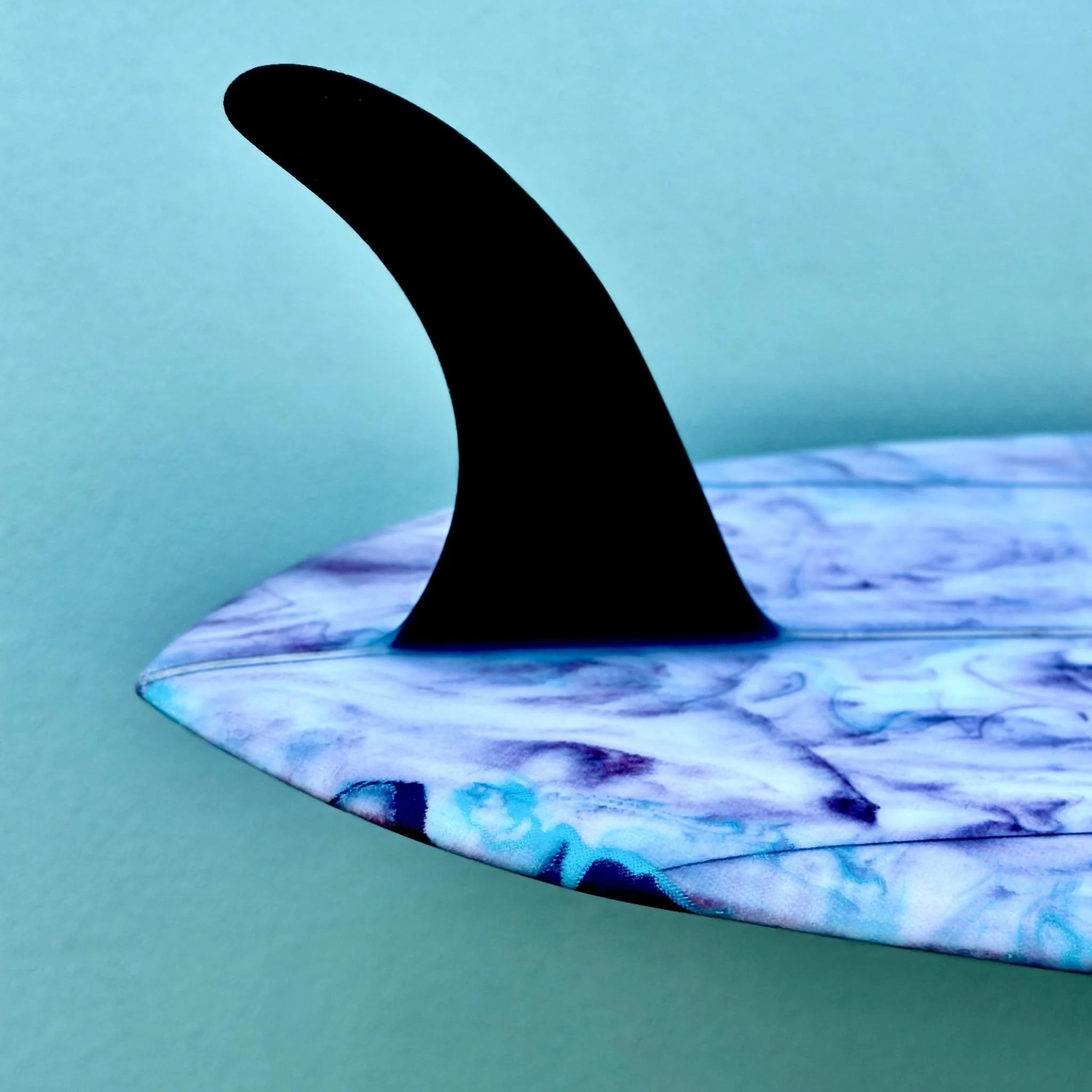 Close-up of a colorful, abstract paper art sculpture with a black foreground shape, textured blue and purple hues, set against a light turquoise background.