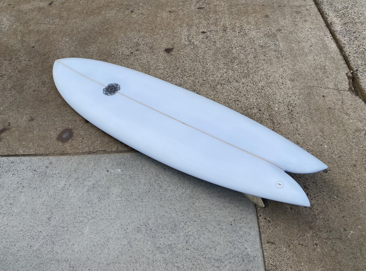 Two white surfboards lying on the ground, one on a concrete surface and the other on a brown section of pavement.