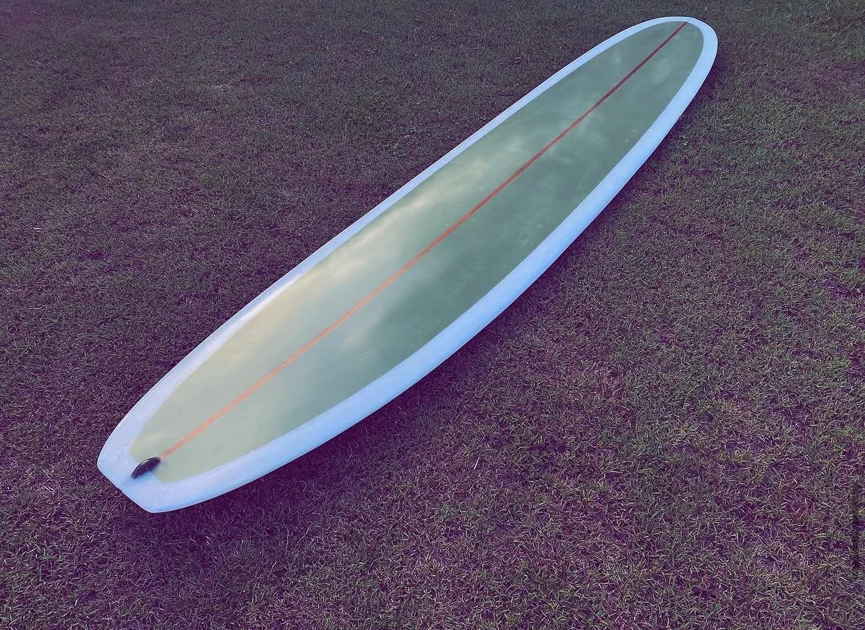 A stand-up paddleboard lies on grass, with a red line running down its center and a small black loop at the front.