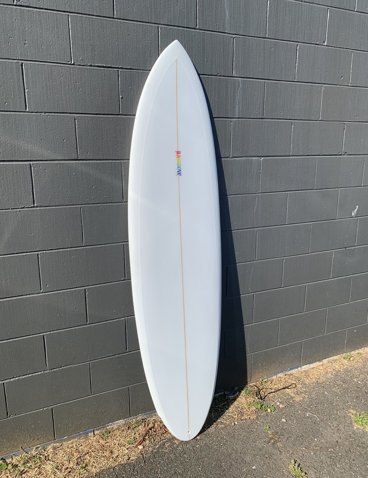 A white surfboard leaning against a dark gray brick wall outside on a sunny day.
