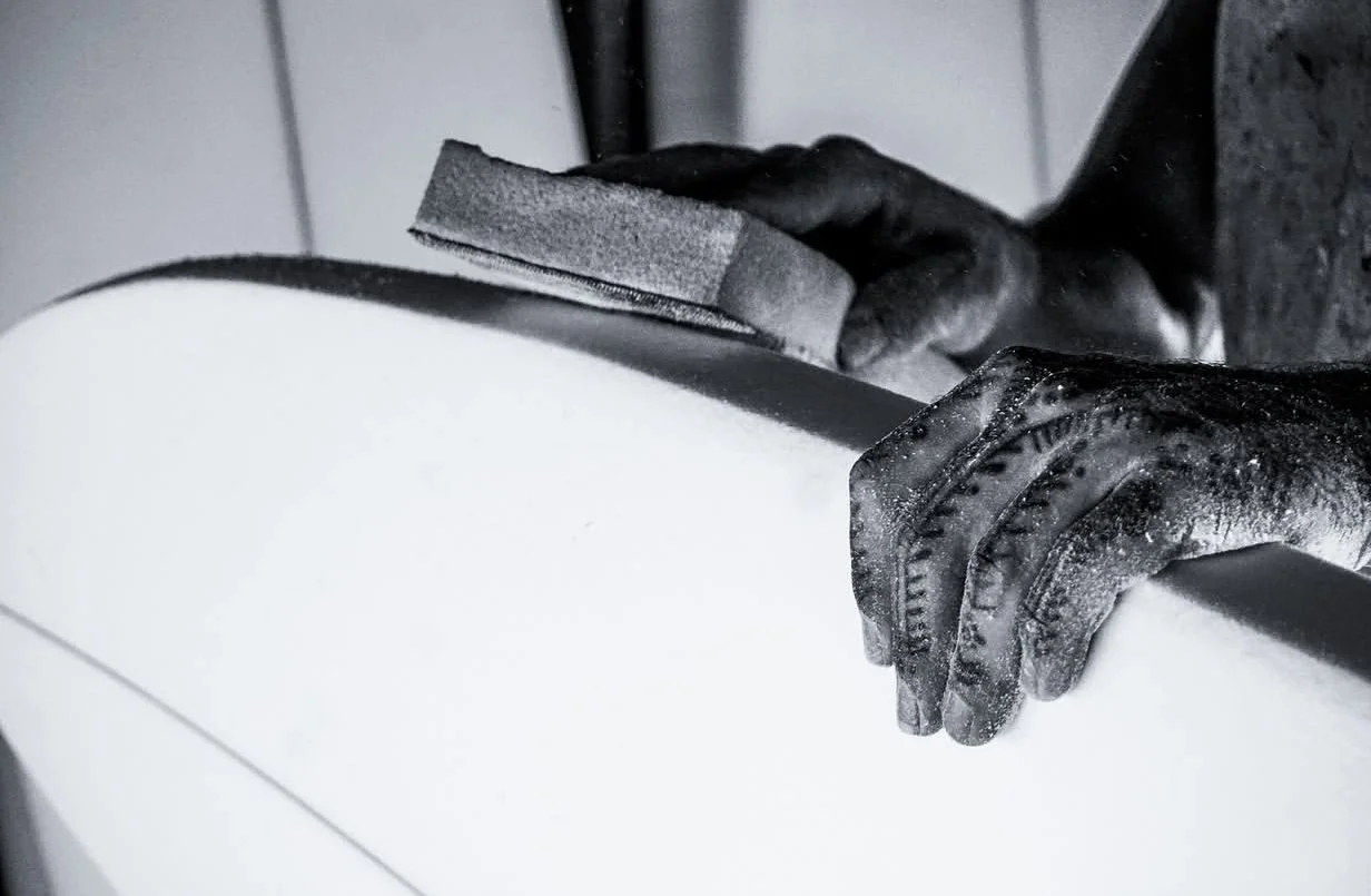 Hands wearing black gloves grinding a piece of material, possibly foam or rubber, on a surface.