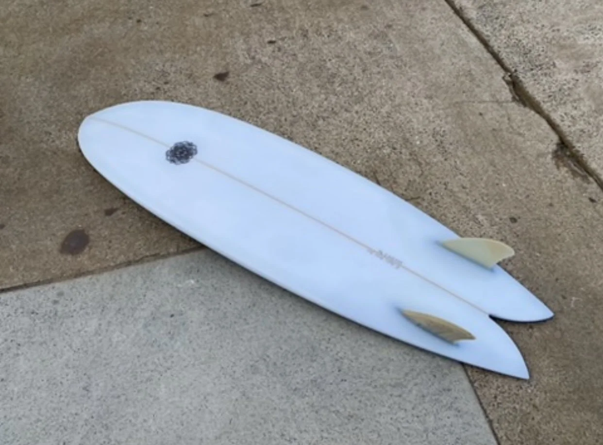 Two white surfboards with beige fins lying on a concrete sidewalk.