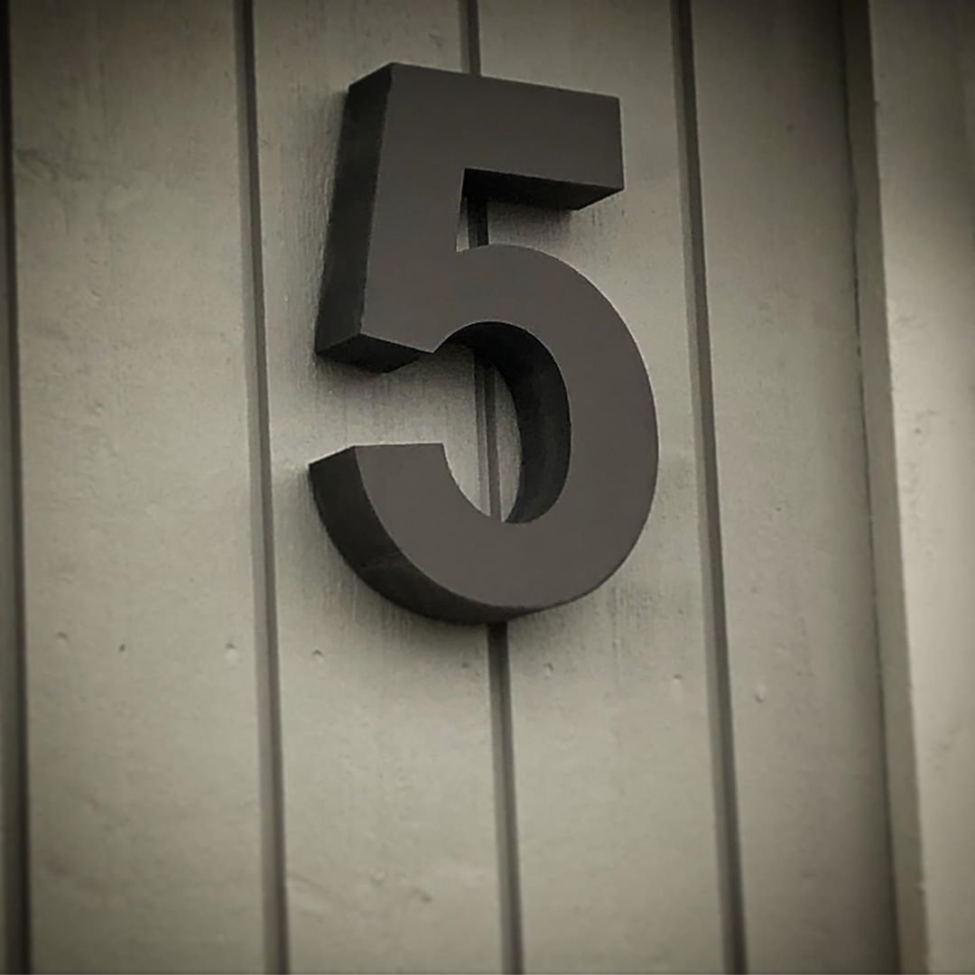 Talonumero 5 tummanharmaa teräksessä vaalealla kivi- ja betonijulkisivulla