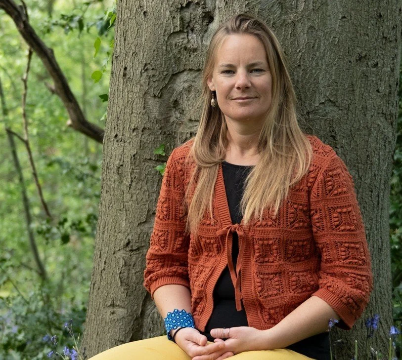 Mareike Ringena, Bristol therapist, seated calmly against a tree trunk with bluebells around her