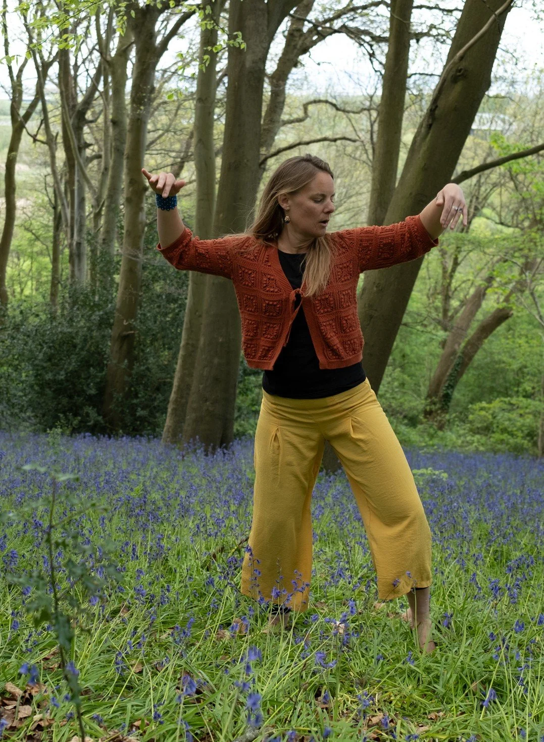 Mareike Ringena, Dance Movement Psychotherapist, moving barefoot among bluebells in a woodland, arms raised mid-movement