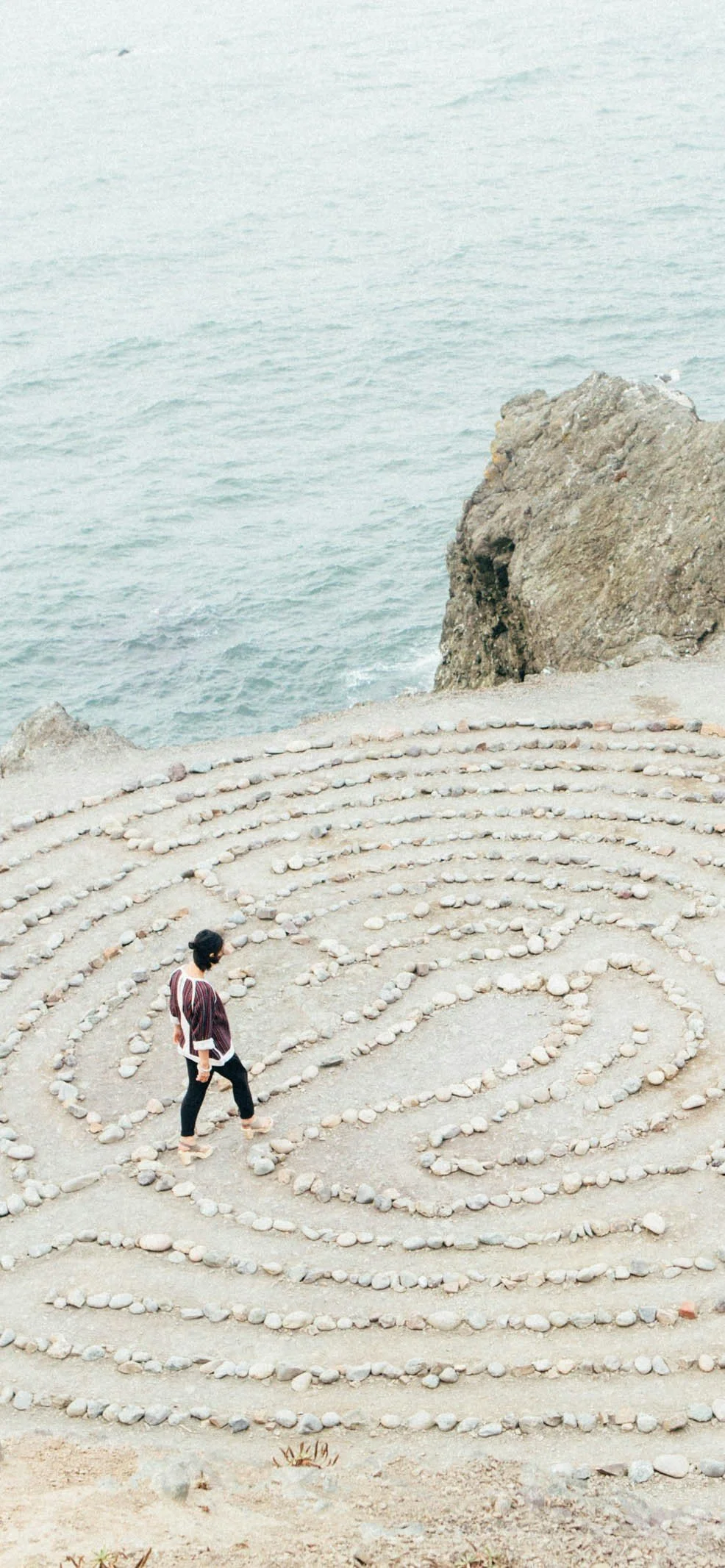A person slowly walking a stone labyrinth on a clifftop beside the sea