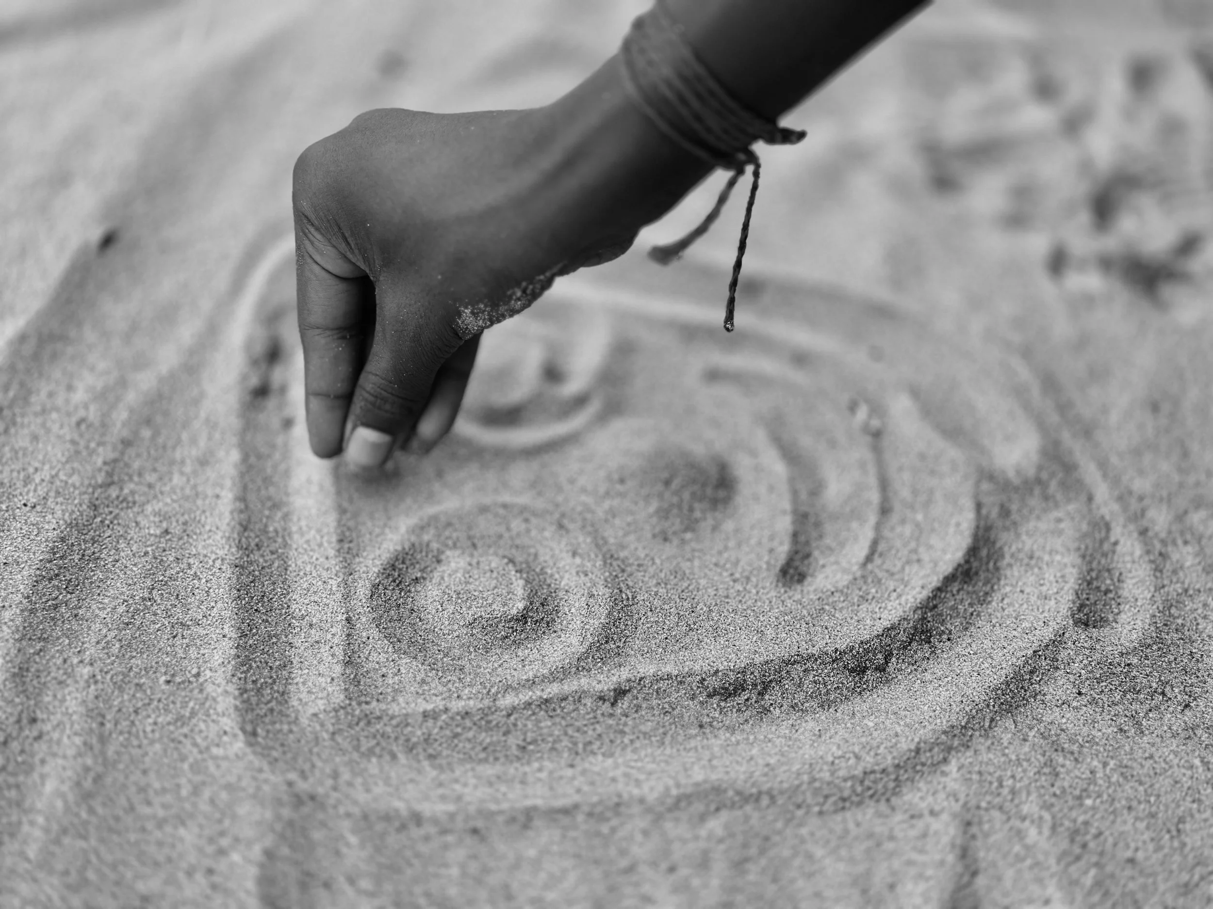 A hand tracing spiral patterns into sand, in black and white