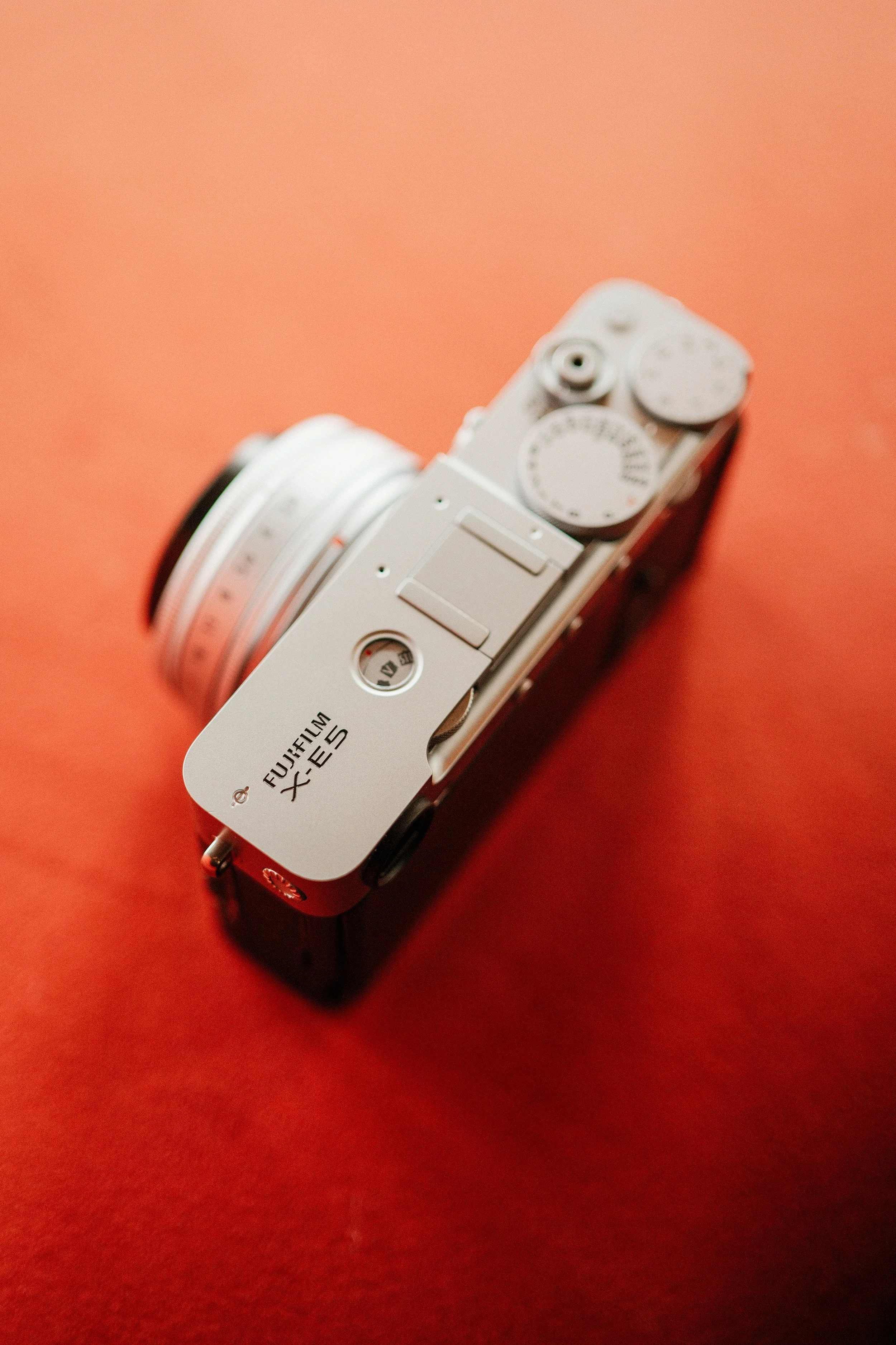 A mirrorless Fujifilm X-series camera with a silver top and black body, placed on a red surface, viewed from an overhead angle.
