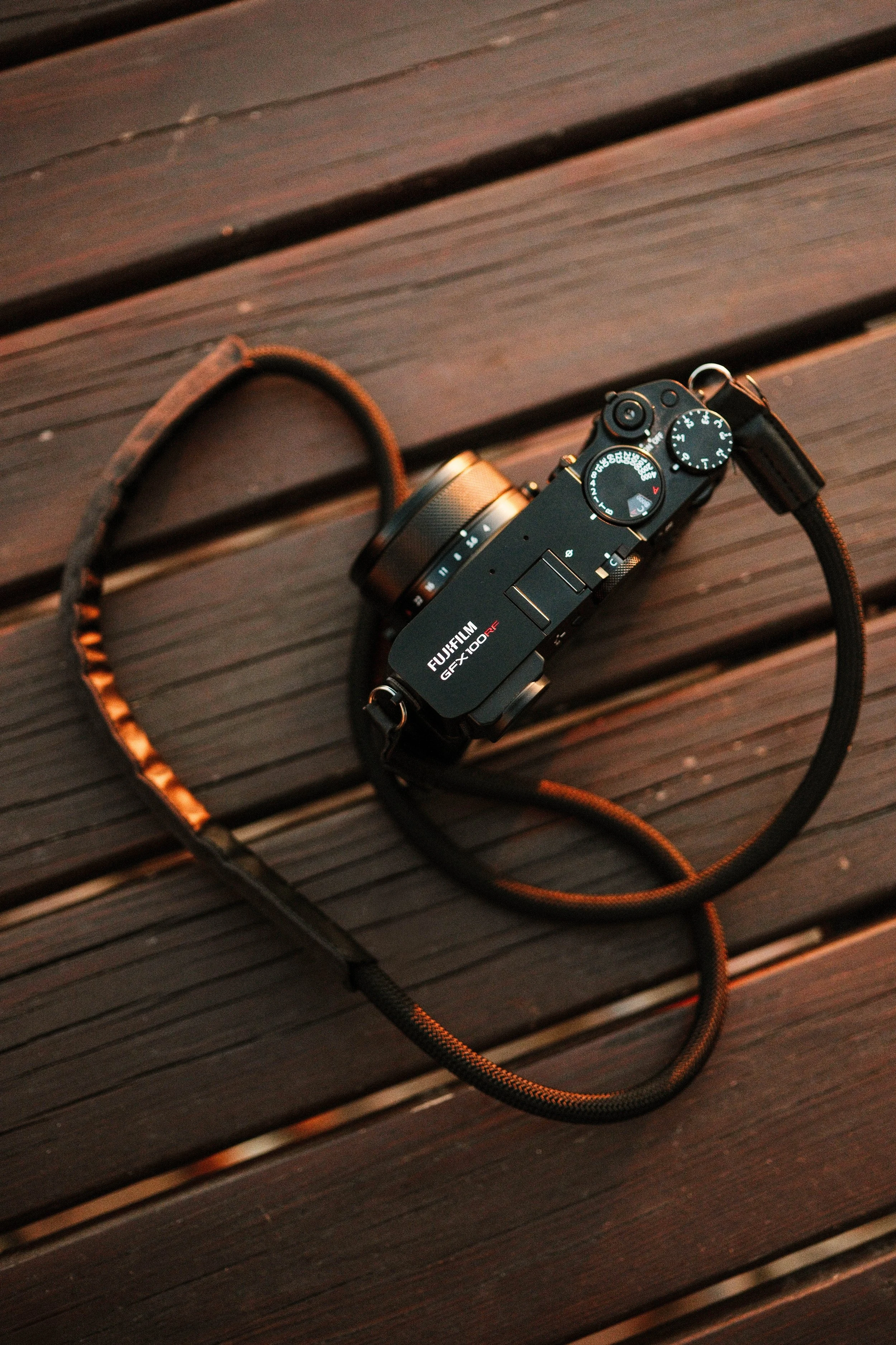 A Fujifilm digital camera with a lens and a black strap resting on a wooden bench.