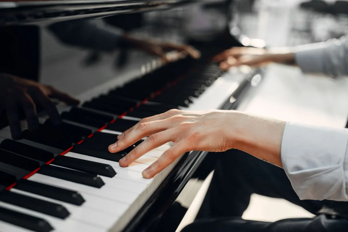 Close-up of a person's hands playing a grand piano, with a reflection of the hands on the polished black surface.