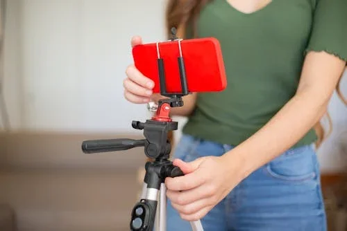 Person wearing a green shirt using a tripod to hold a smartphone for recording or photography.