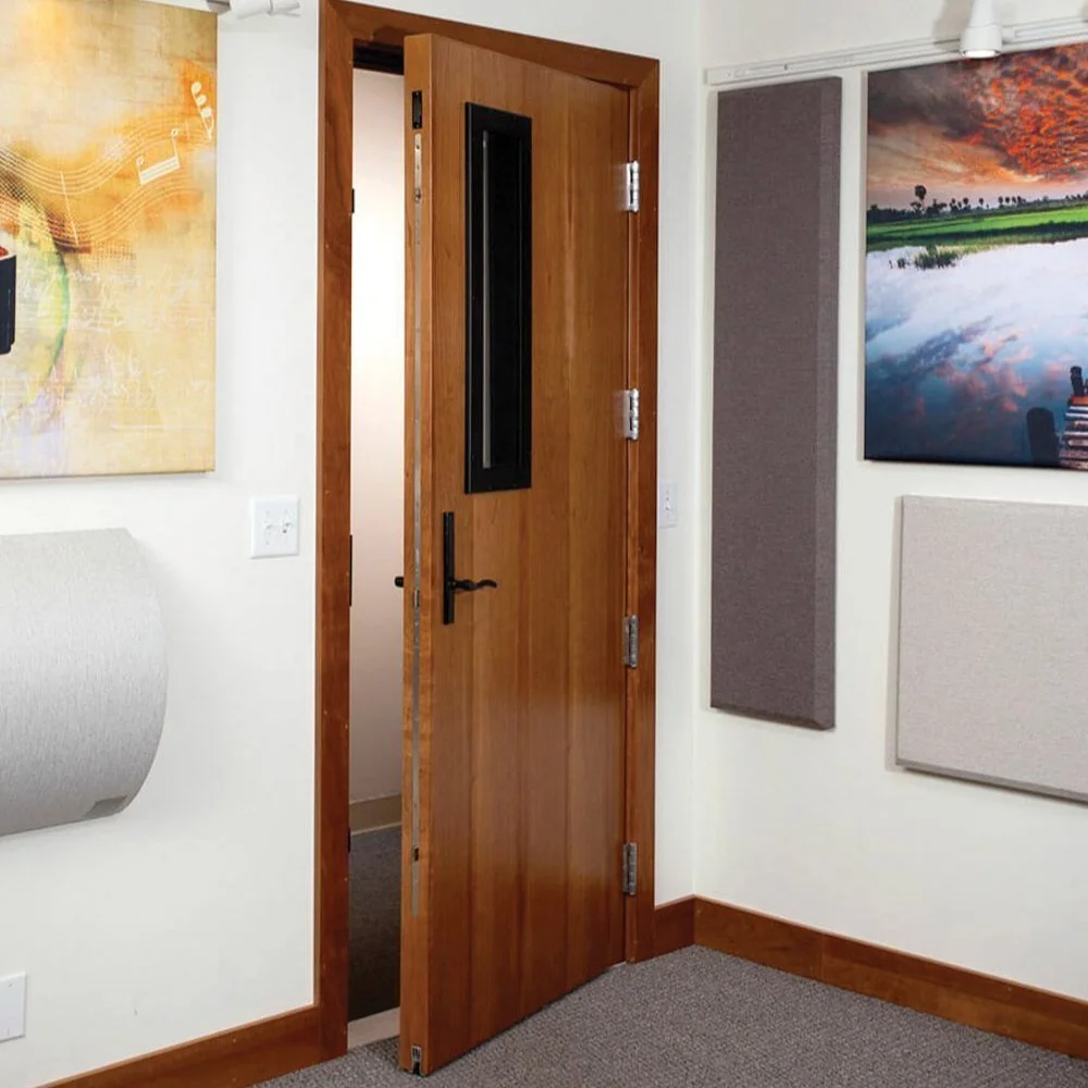 An interior room with a wooden door slightly open, showing a hallway. The walls are decorated with colorful artwork and acoustic panels. The room has a carpeted floor and white walls with wooden trim.