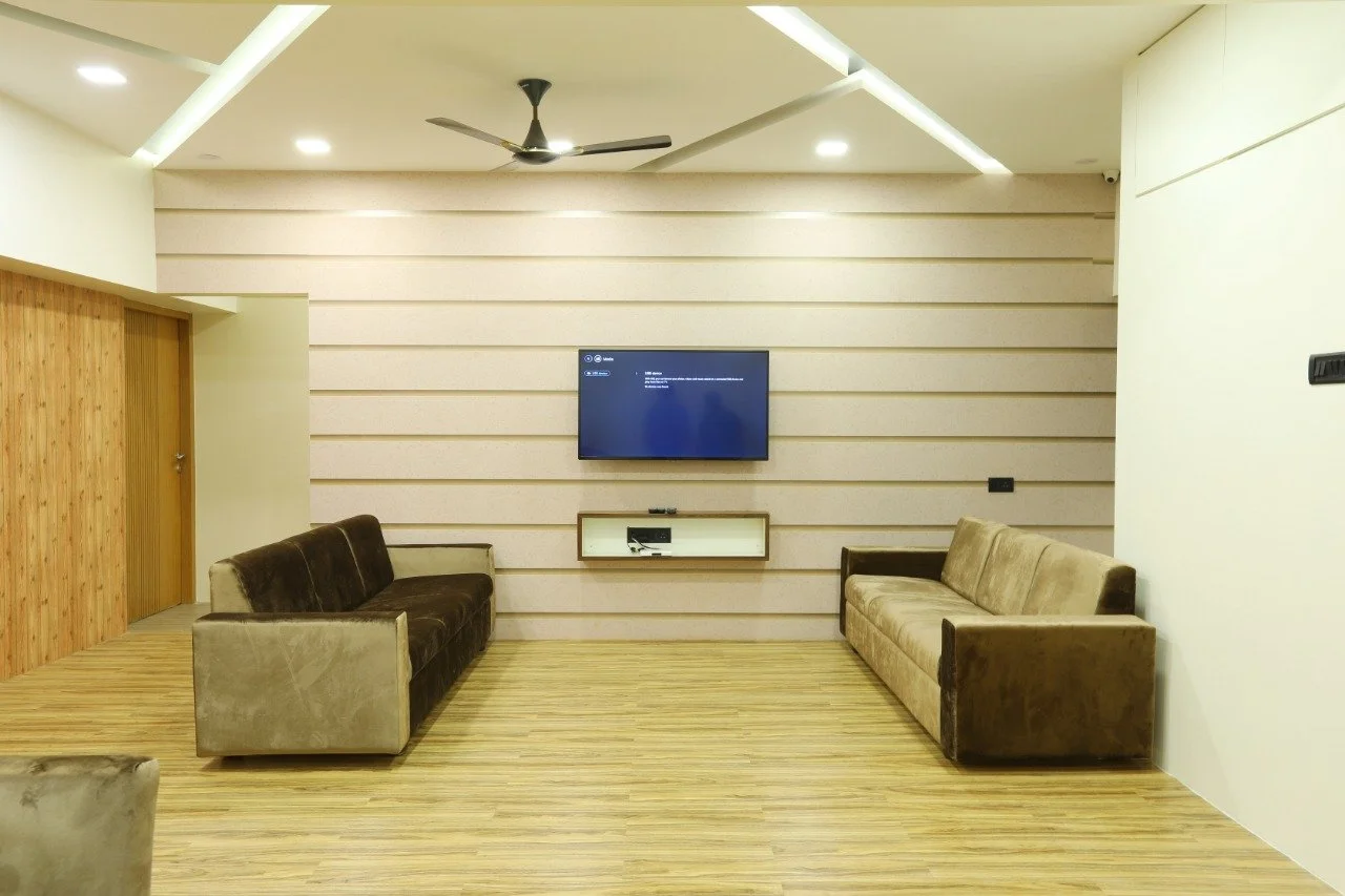 Living room with beige and brown sofas, a mounted flat-screen TV, wood-paneled wall, and ceiling lights.