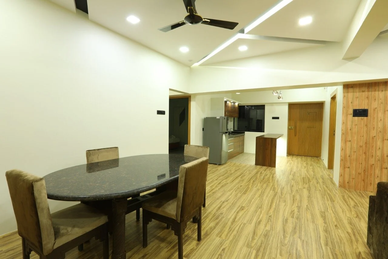 Open-concept living space with a dining table with four upholstered chairs, a kitchen area with a refrigerator, sink, and countertop, wood flooring, and a ceiling fan.