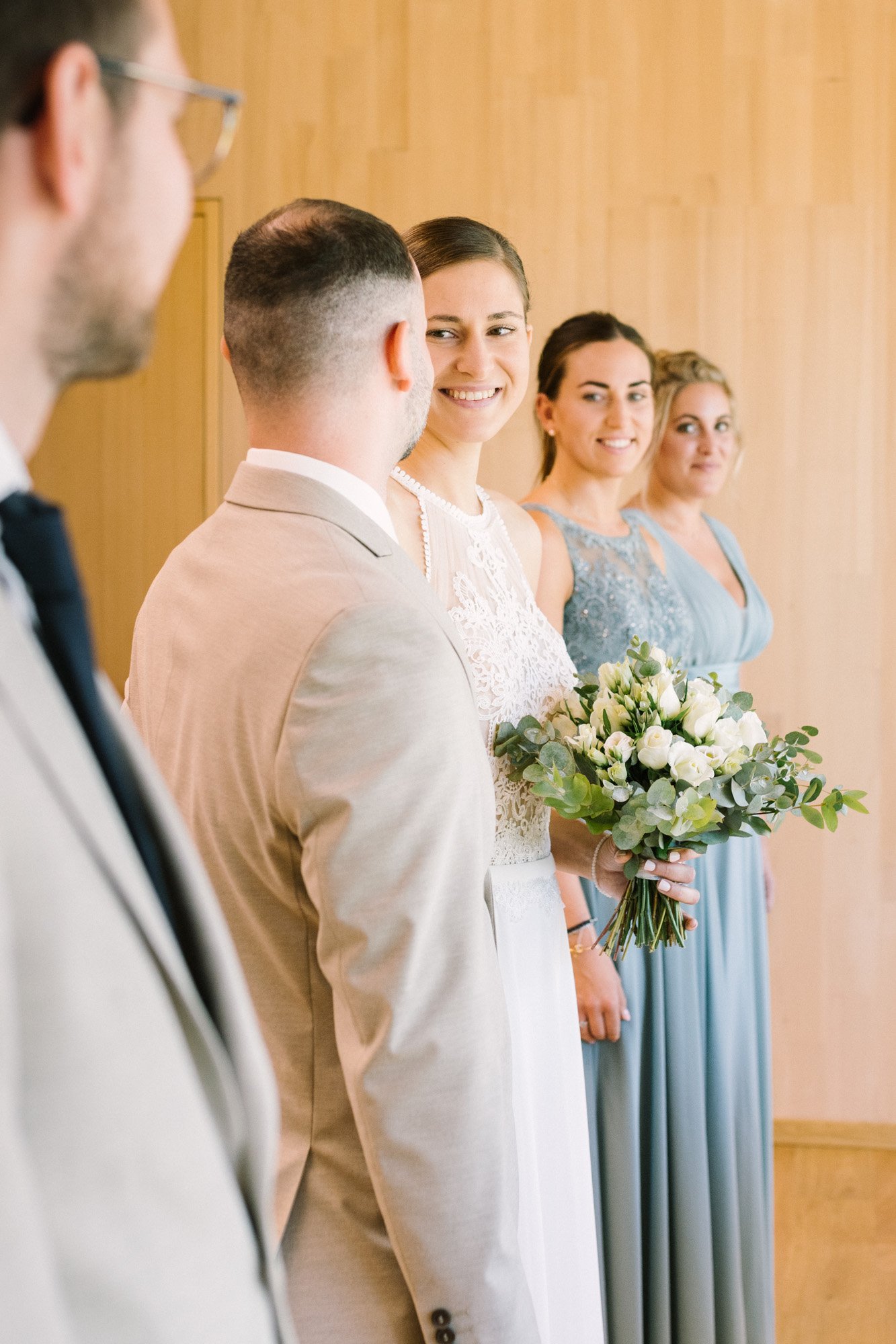 Braut mit Brautstrauß bei einer Hochzeit, im Hintergrund sind drei Frauen in eleganten Kleidern, alle lächeln.