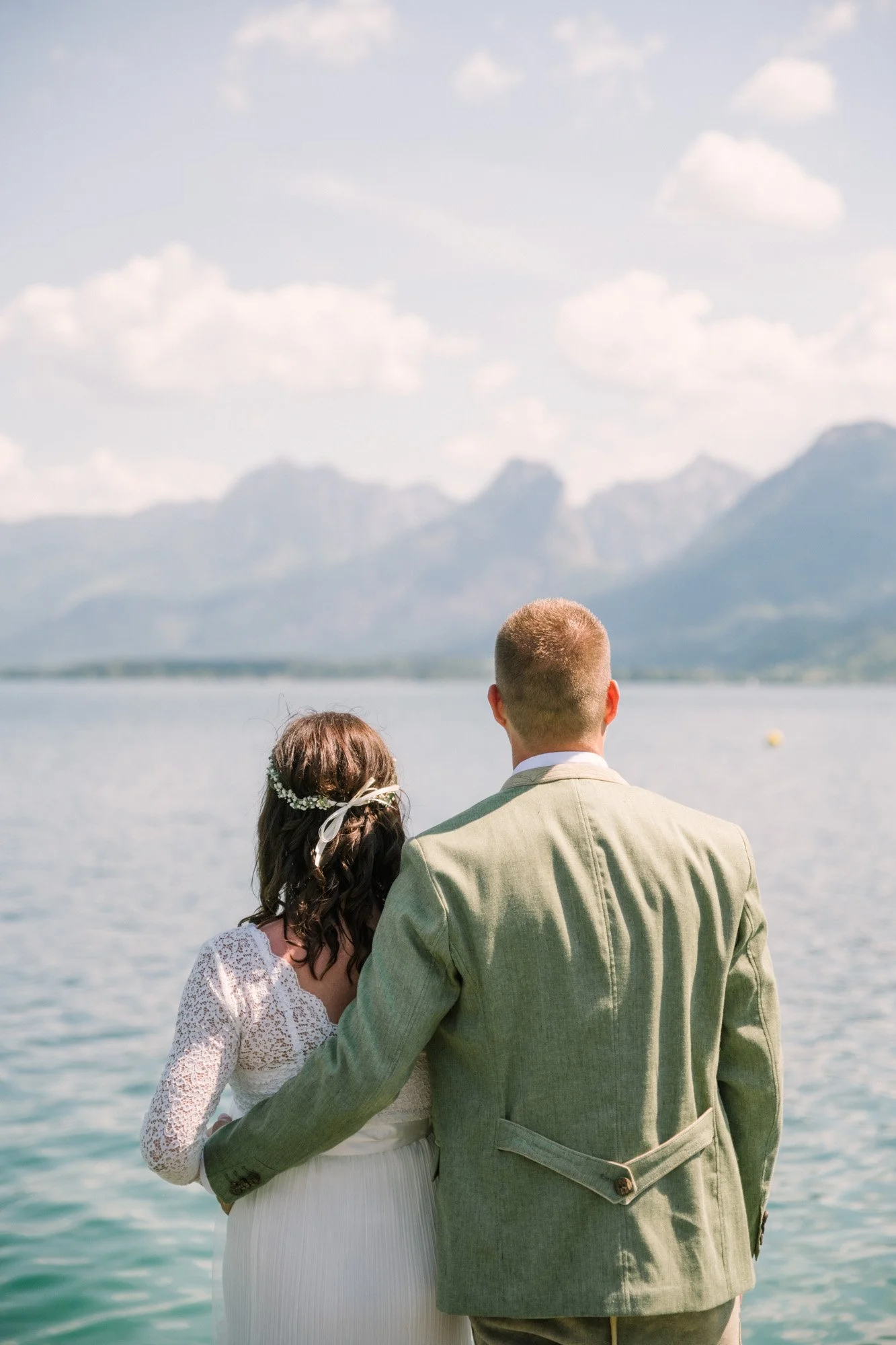 Ein Paar sitzt am Wasser, mit Blick auf Berge, bei einer Hochzeitszeremonie im Freien.