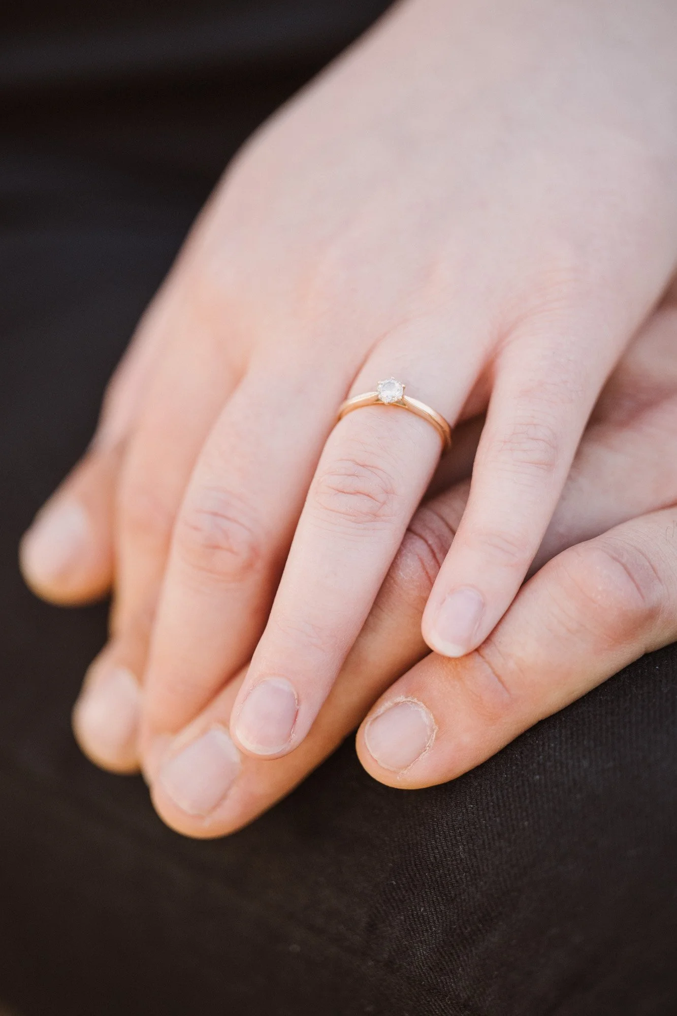 Nahaufnahme eines Handrings mit Diamanten auf einem Finger, die Hand liegt auf einem schwarzen Stoff.