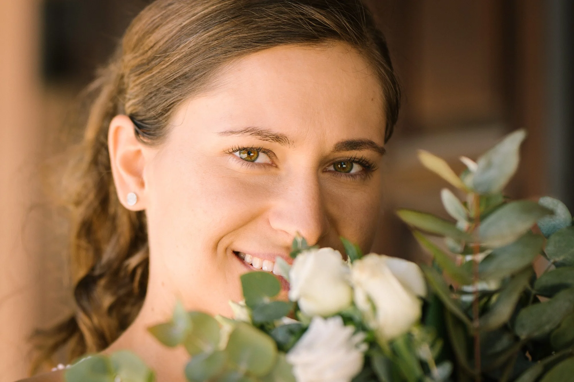 Eine lachende Frau mit braunen Haaren hält einen Blumenstrauß aus weißen Rosen und Eucalyptus-Blättern.