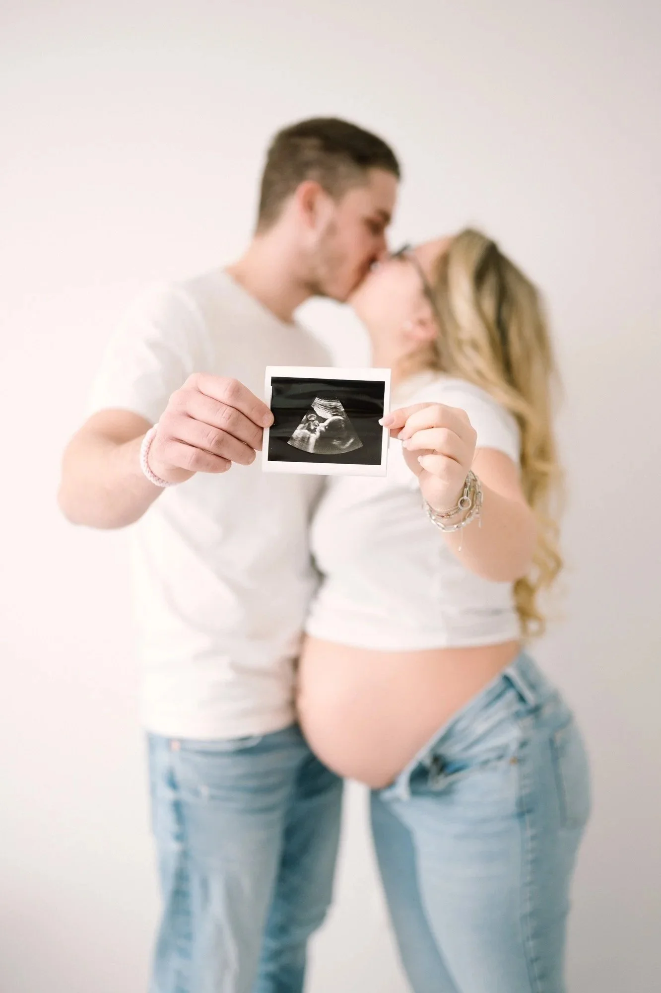 Ein schwangeres Paar, das sich küsst, hält ein Ultraschallbild ihres Babys in den Händen.