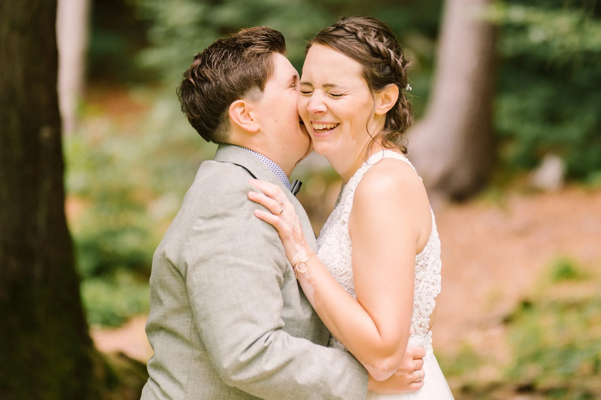 Ein Brautpaar in einem Wald, das sich küssend und lachend umarmt.