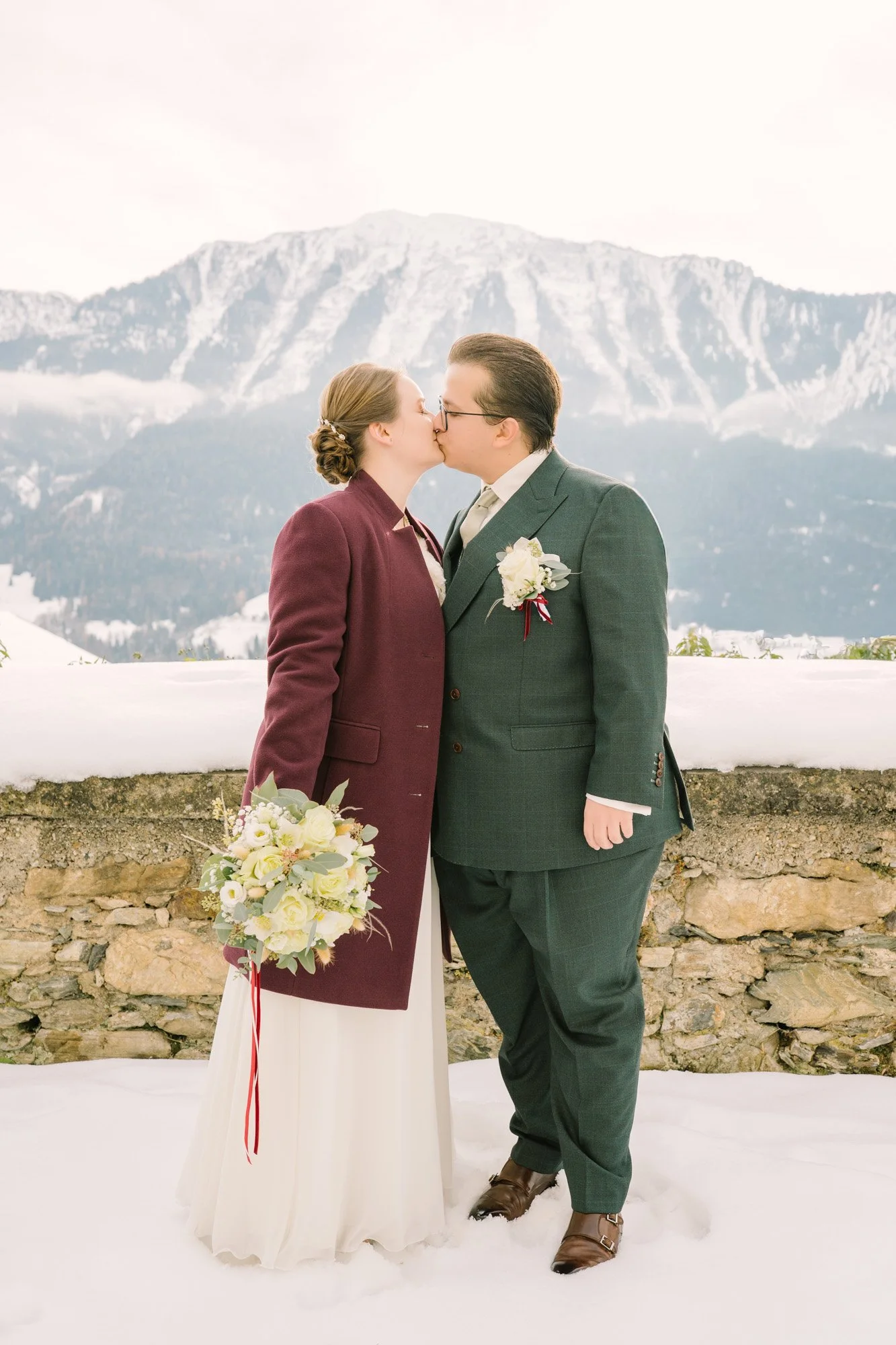 Ein Paar bei ihrer Hochzeit küsst sich im Schnee vor einer Bergkulisse.