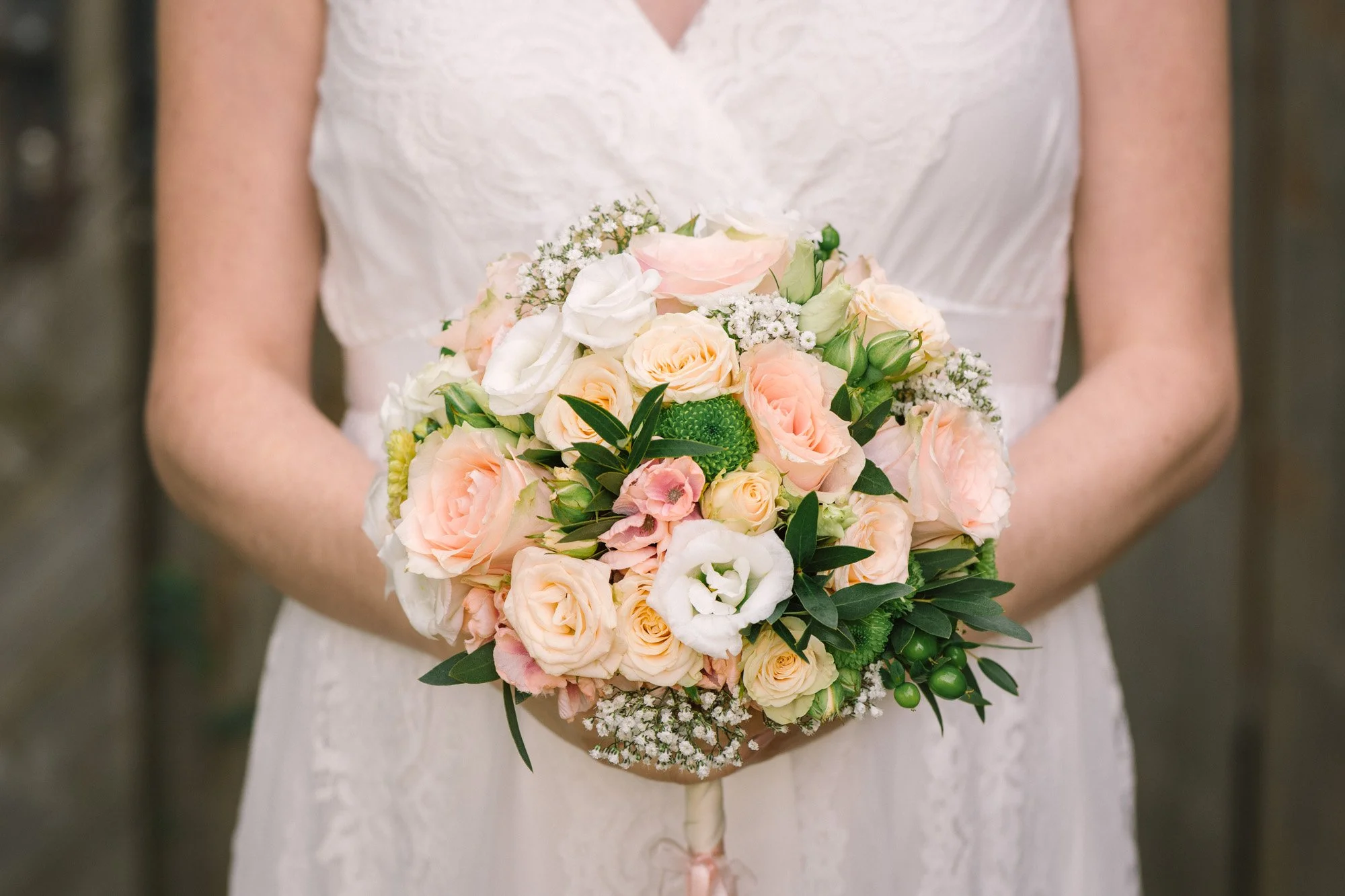 Eine Frau in einem weißen Kleid hält einen Blumenstrauß aus hellrosa, weißen und cremefarbenen Blumen mit grünen Blättern