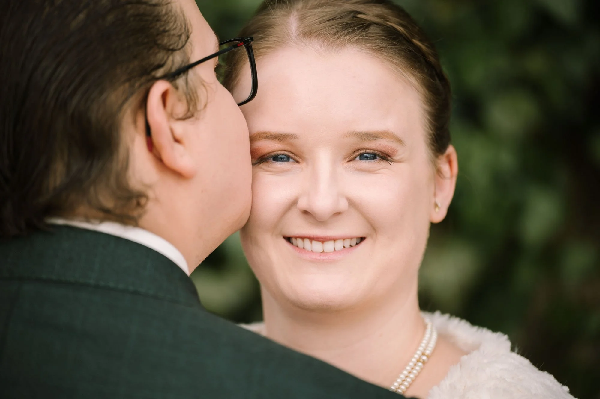 Ein junges Paar bei einer Hochzeit, der Mann küsst die Frau auf die Wange, sie lächelt glücklich.
