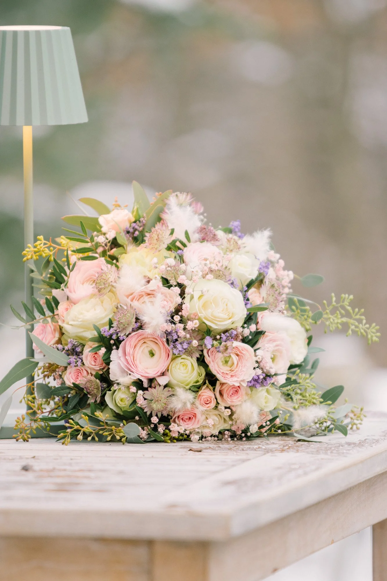 Blumenstrauß mit weißen und rosa Rosen, lilafarbenen und weißen Blüten, grünem Laub, auf einem Holztisch, im Hintergrund unscharf.