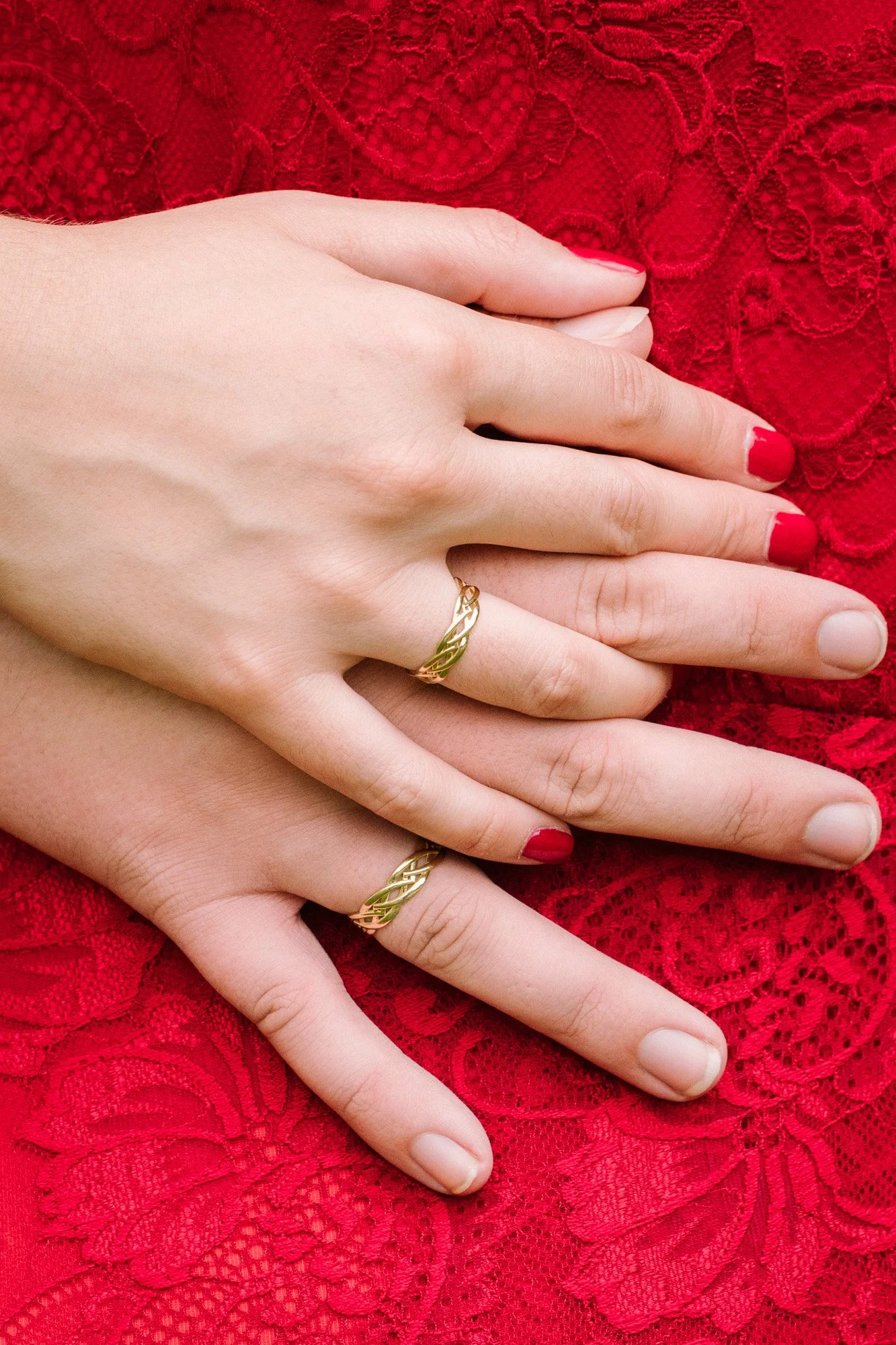 Zwei Hände mit goldenen Ringen auf den Fingern, auf rotem Spitzenstoff
