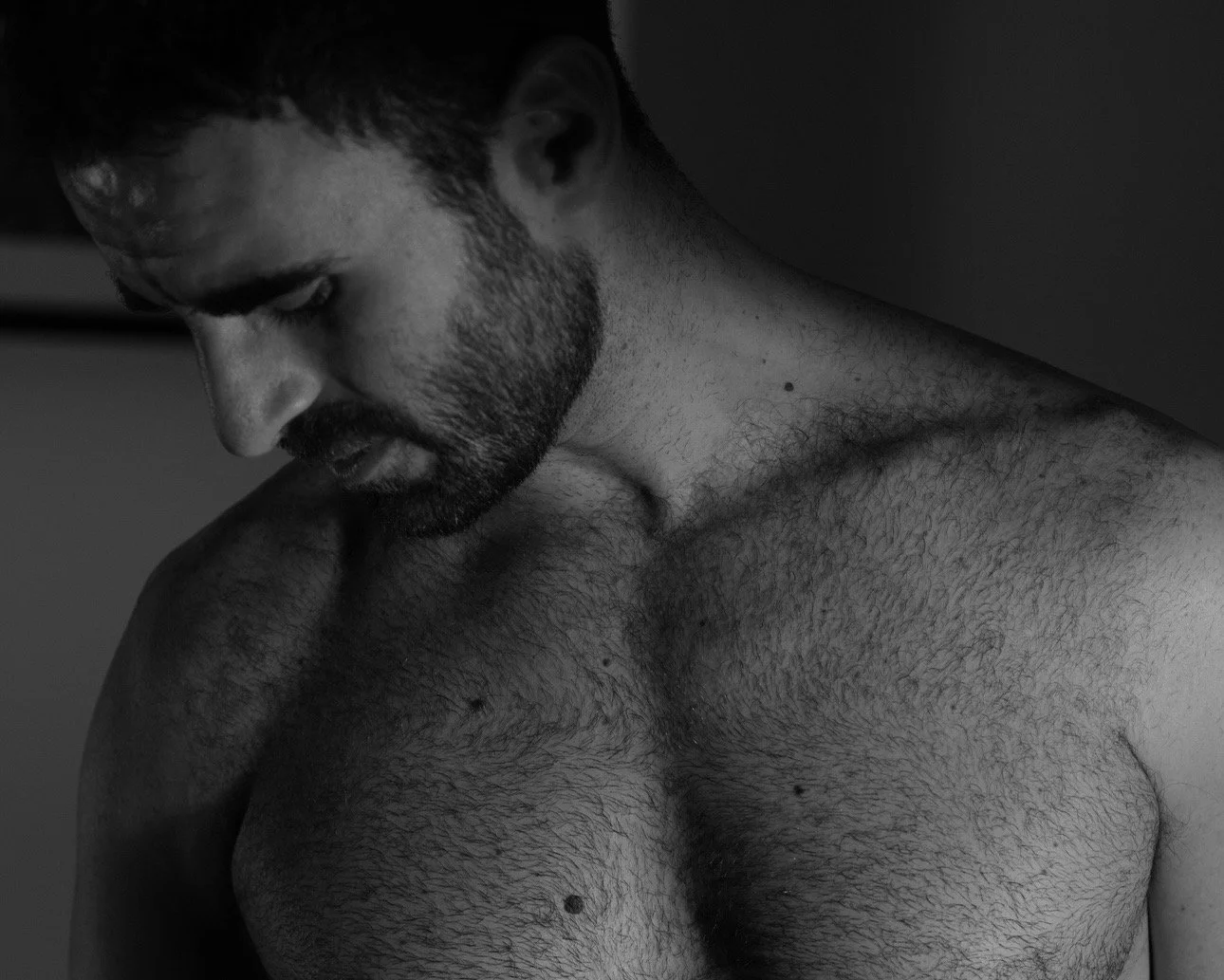 A shirtless man with a beard looking downward in a black and white photo.