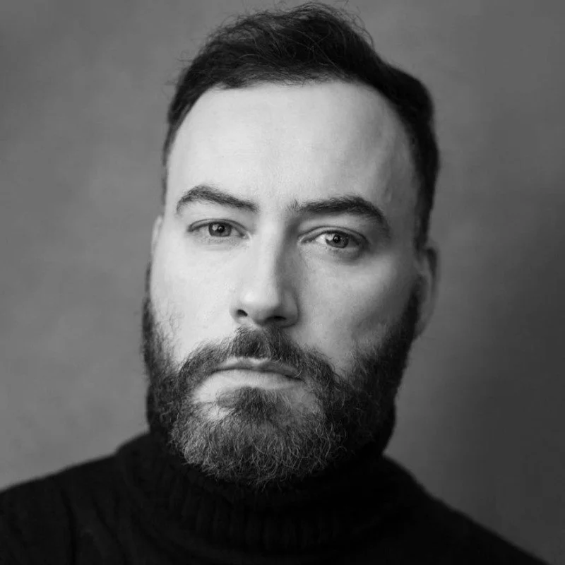Black and white portrait of a man with a beard and short hair, wearing a black turtleneck.
