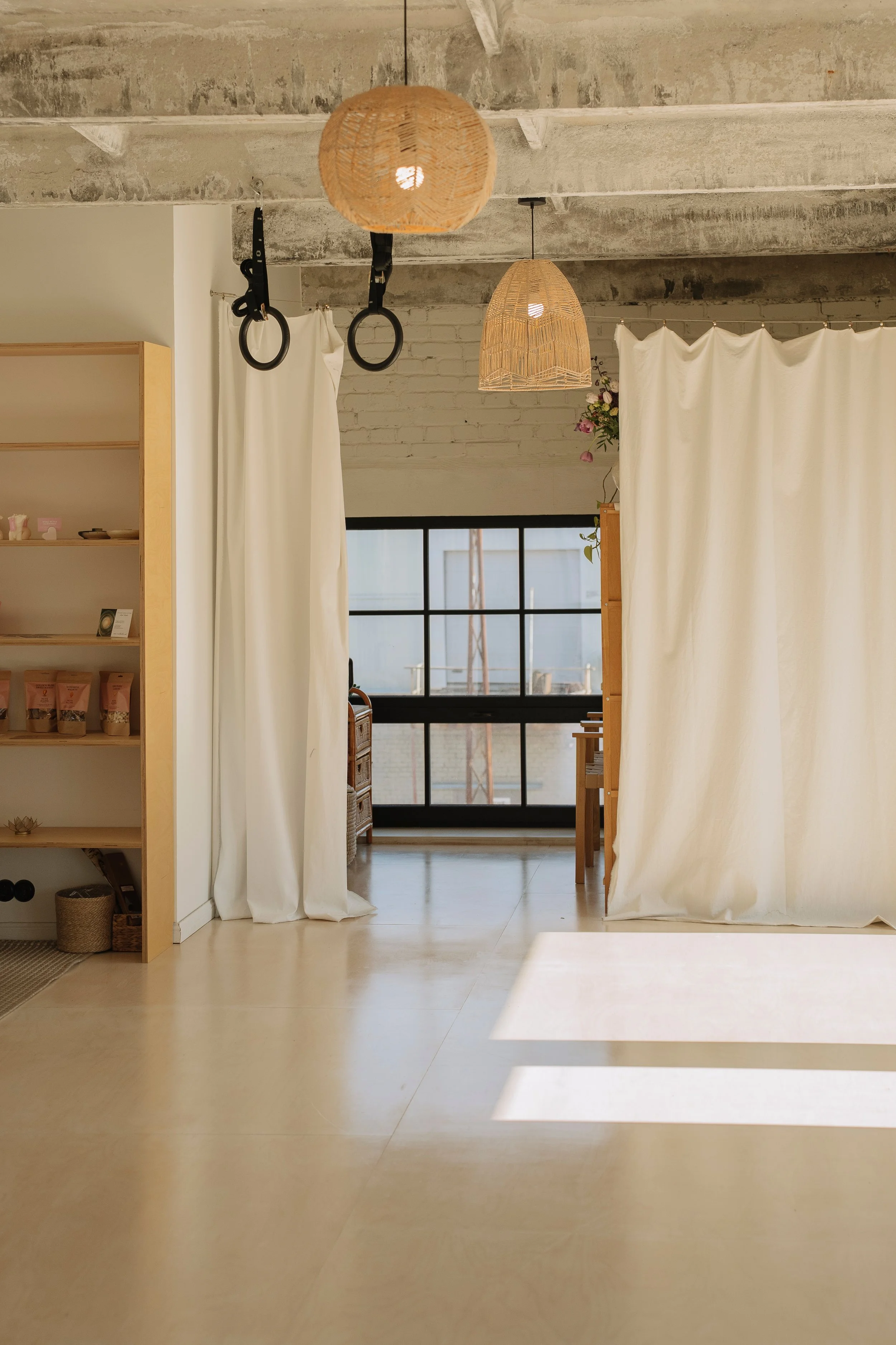 Interior room with a concrete ceiling, wood shelving, white curtains, and a large window, illuminated by natural light.