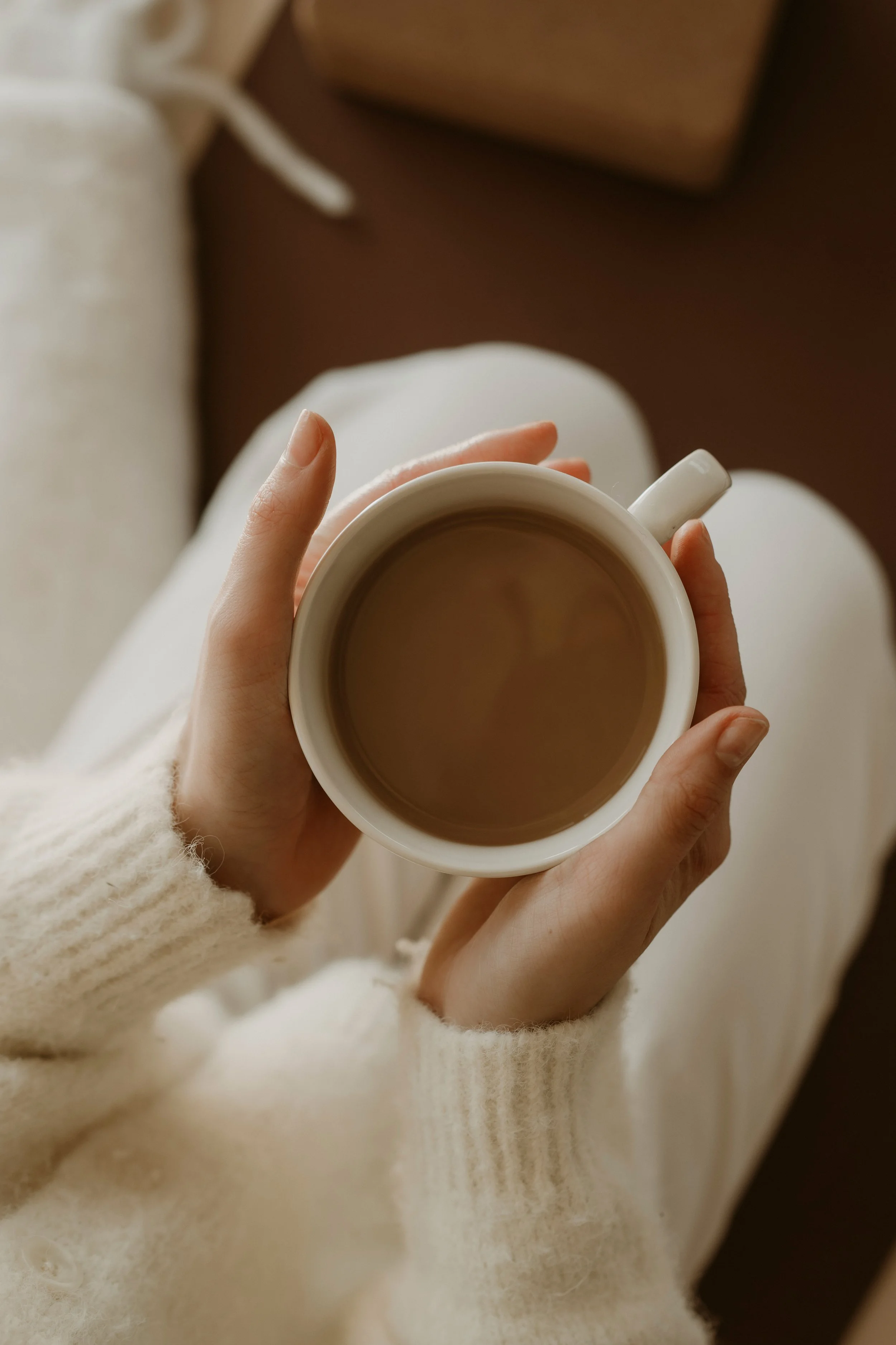 Person holding a white mug filled with coffee, wearing a cozy cream-colored sweater.