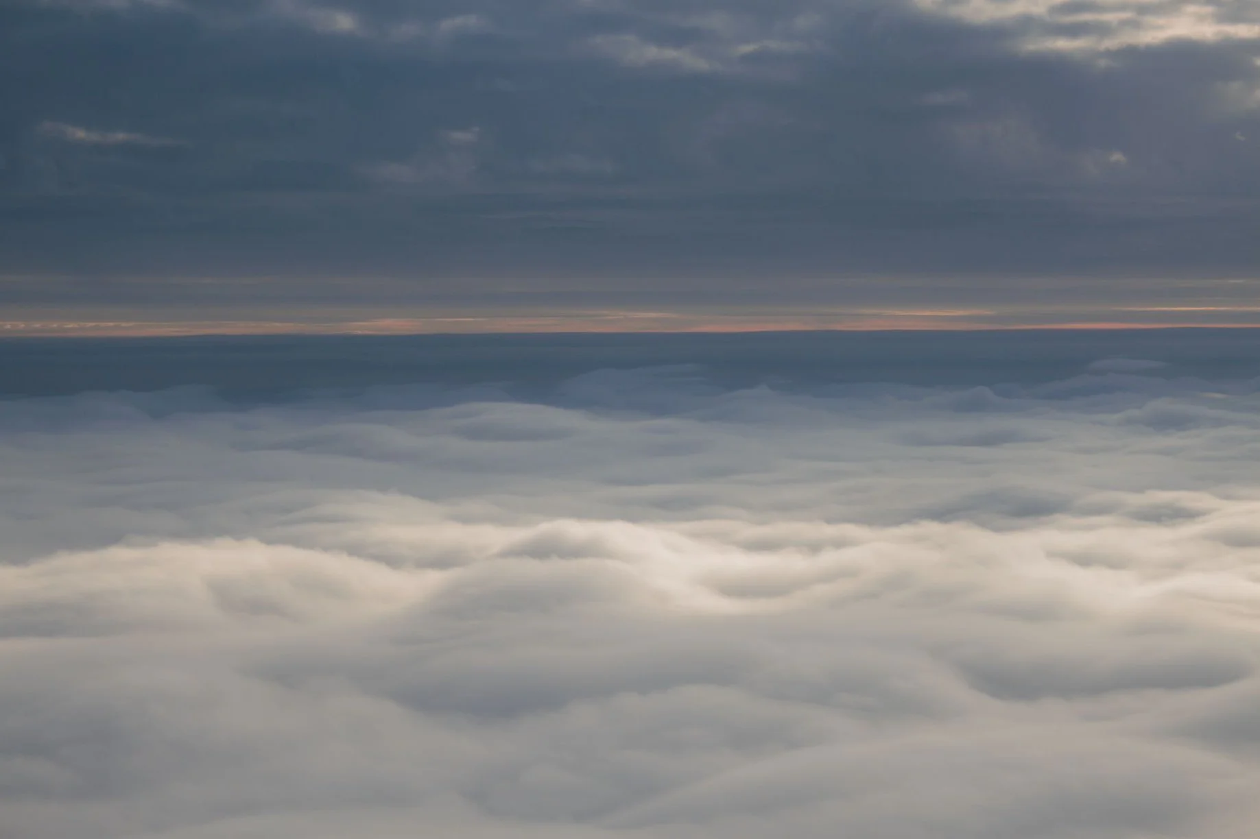 A view of clouds from above during sunset or sunrise, with dark clouds at the top and lighter clouds below, creating a layered and serene sky scene.