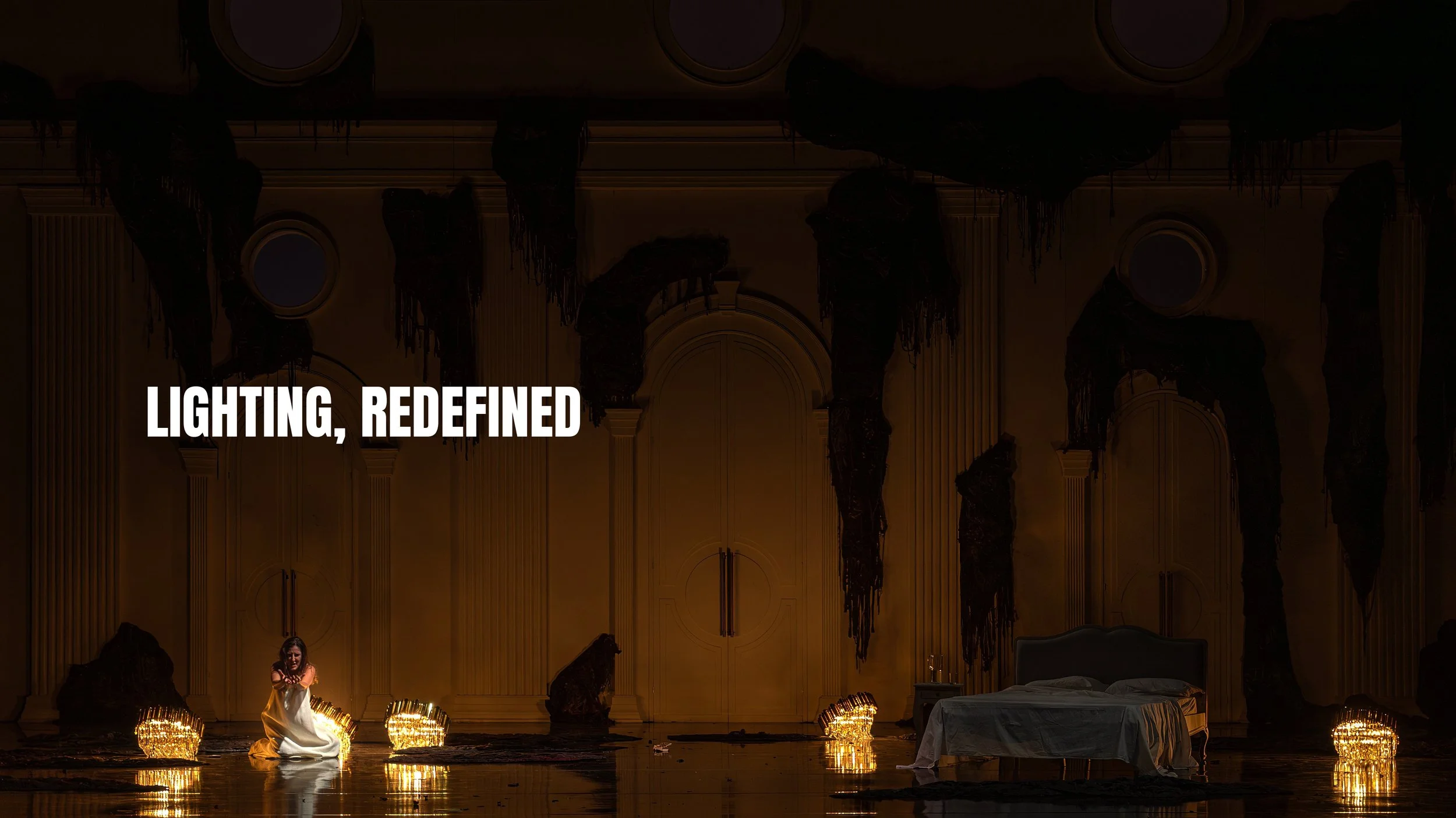 A theatrical stage set with a woman sitting on the floor, illuminated by glowing lights, a bed on the right, and dark drapes hanging from the ceiling. The words 'Lighting, Redefined' are overlaid on the image.