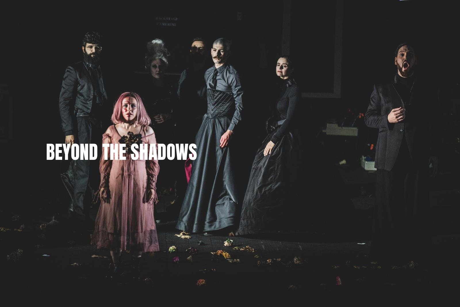 The image shows a group of seven performers on stage, dressed in dark, dramatic clothing. The background is dark, and some stage props are visible. The title "Beyond the Shadows" is overlaid on the left side of the image.