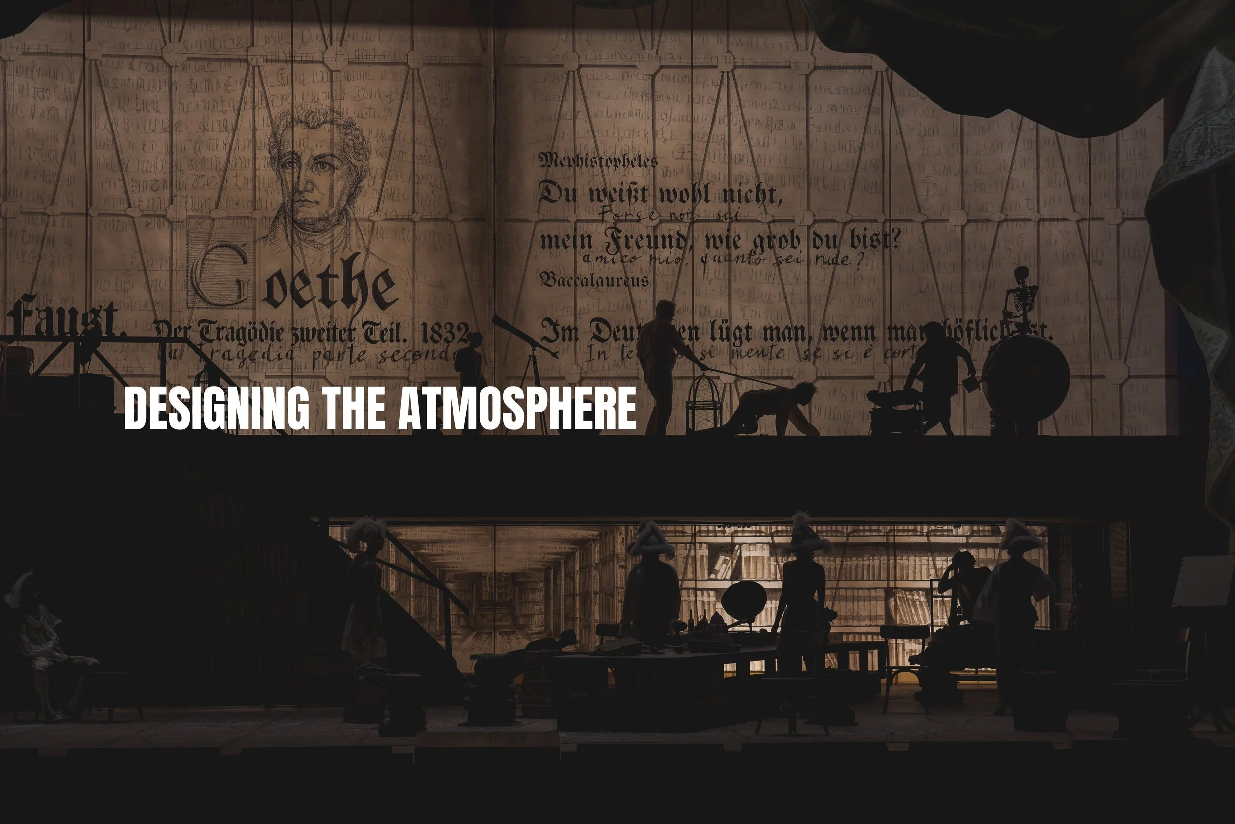 The image shows a theatrical set design scene with silhouettes of people working amidst a backdrop of a large, historical German text and a drawing of Johann Wolfgang von Goethe. The scene is divided into two levels, with the upper level featuring wo