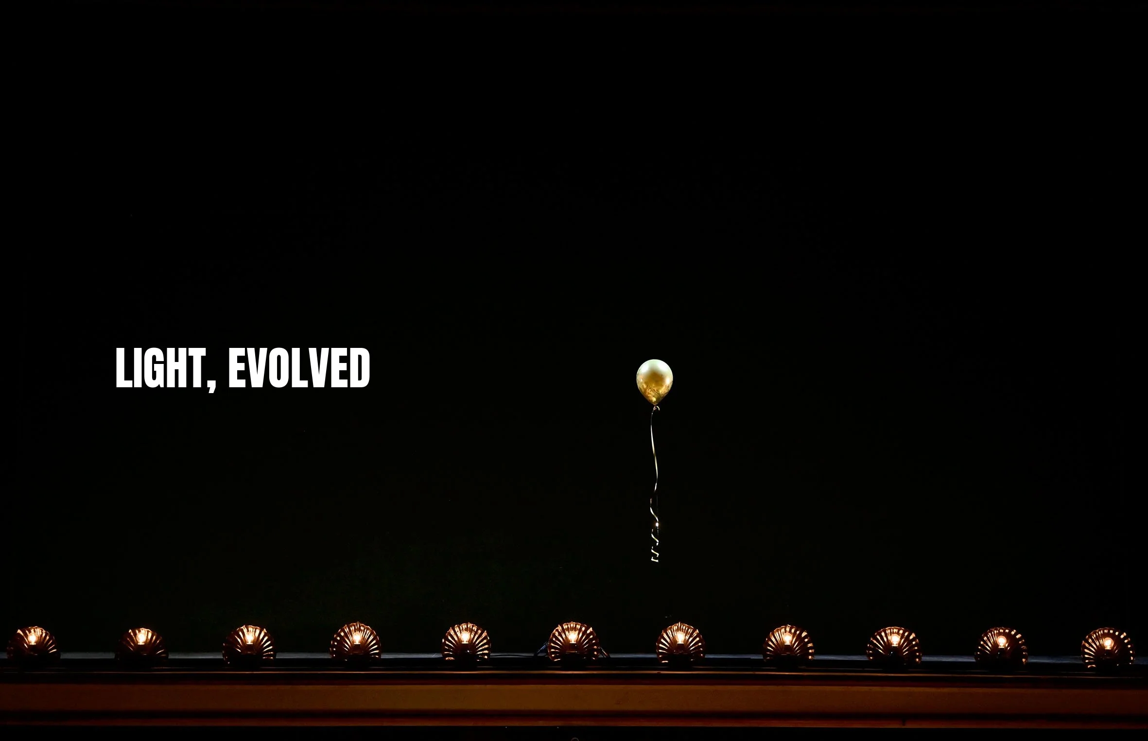 A single white and gold balloon floating above a row of small, illuminated, shell-shaped lights on a dark background. The text 'LIGHT, EVOLVED' is displayed on the left side of the image.