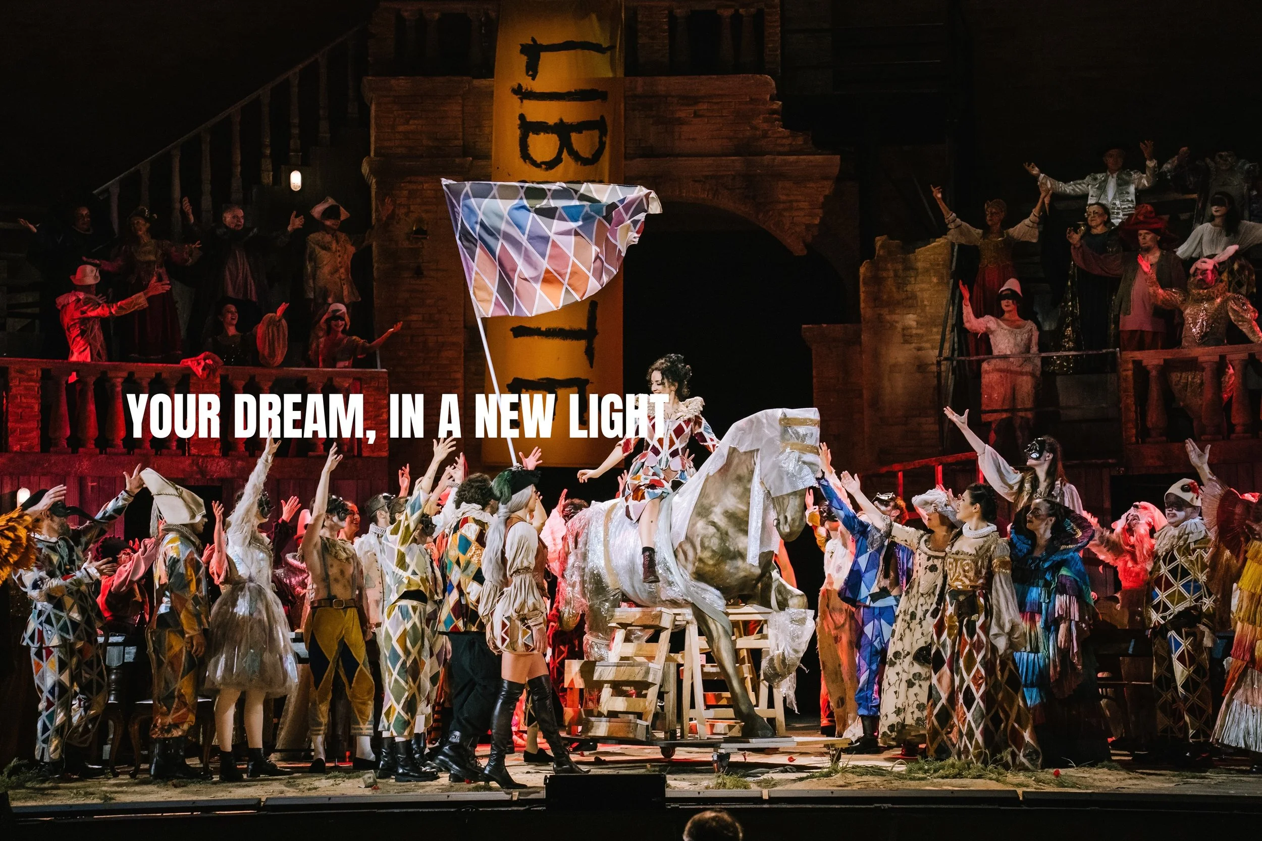 Theatrical scene with performers in colorful costumes, a person on a horse prop, and a large yellow banner with black text. Scene is illuminated with stage lighting, and the text overlay reads 'YOUR DREAM, IN A NEW LIGHT'.