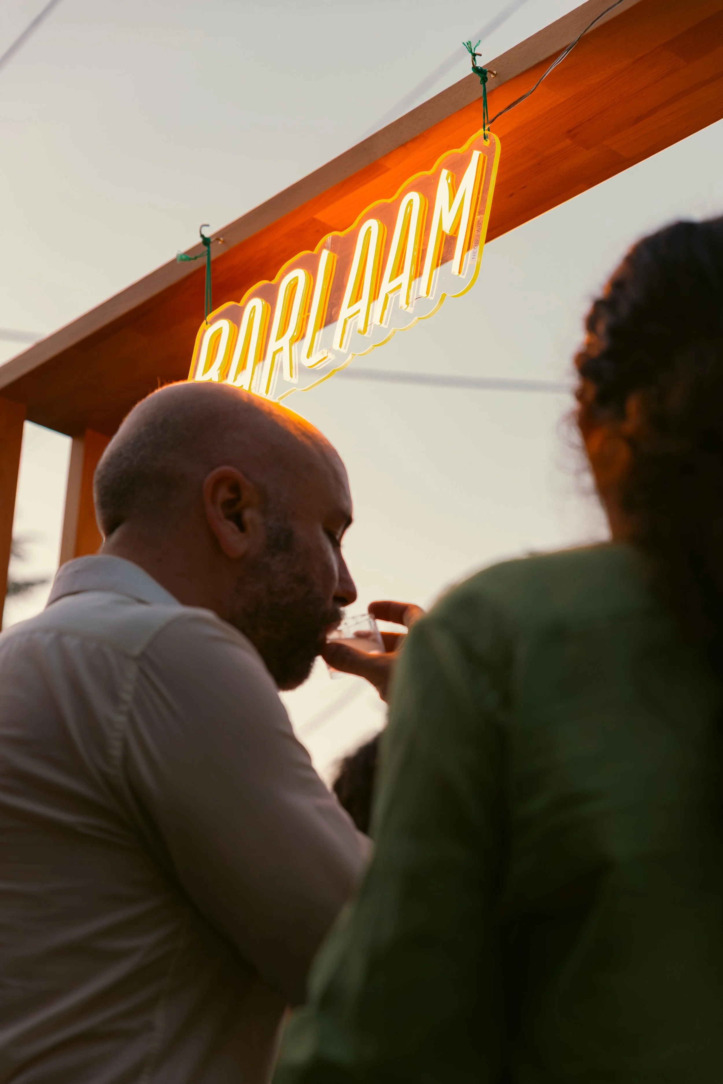 Persone che si godono un momento insieme all'aperto con un cartellone al neon con la scritta 'BIALAHAM' sospeso sopra di loro