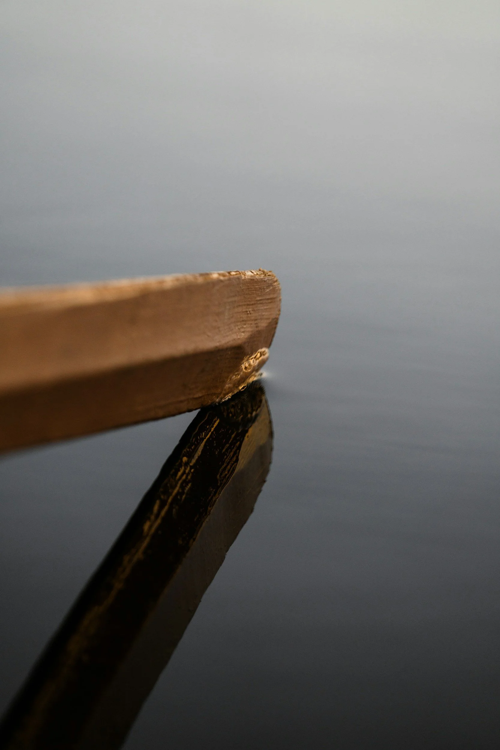 Close-up of a wooden dock edge reflected on calm water against gray sky