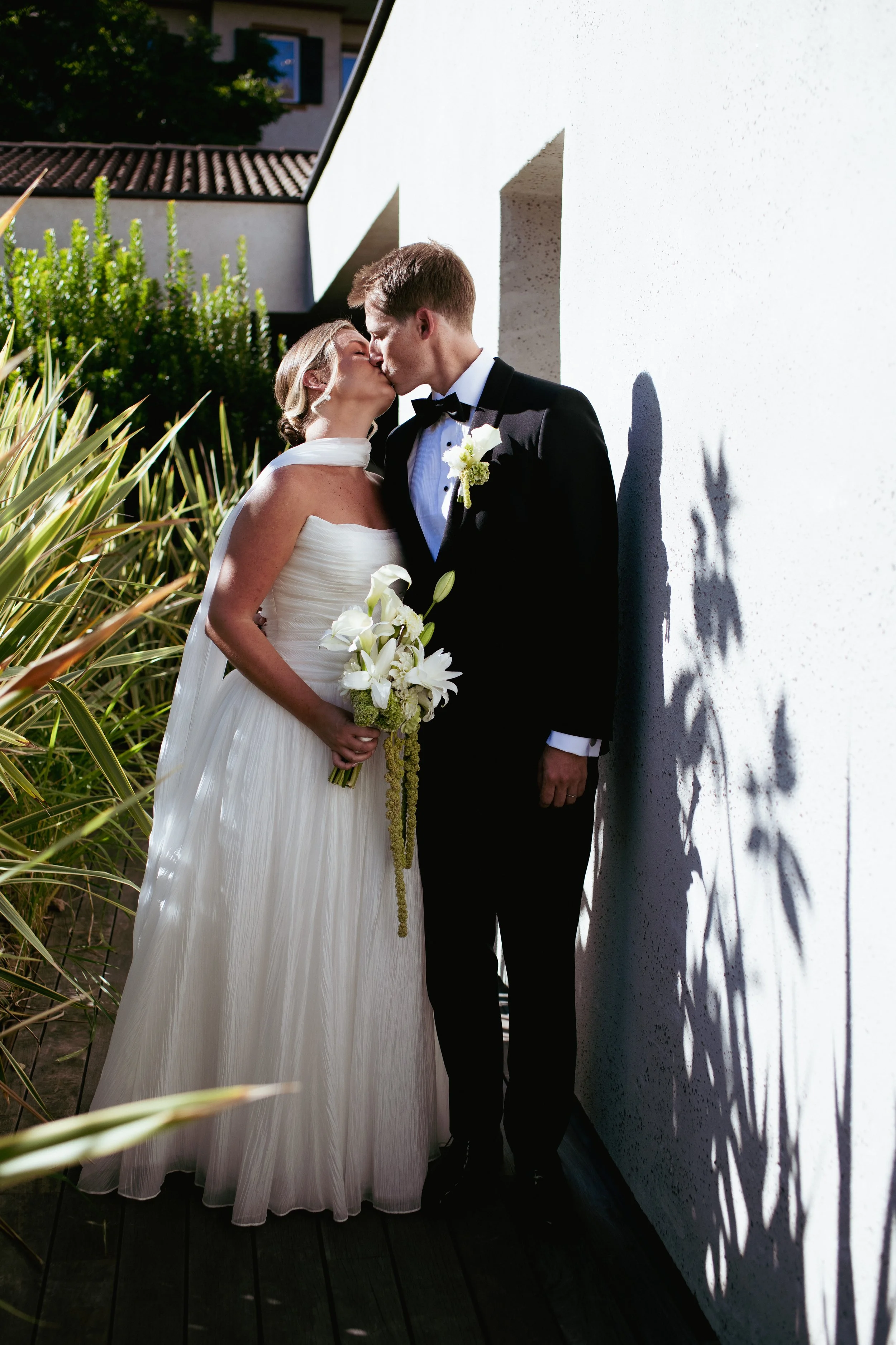 A bride and groom sharing a kiss outdoors on a sunny day.