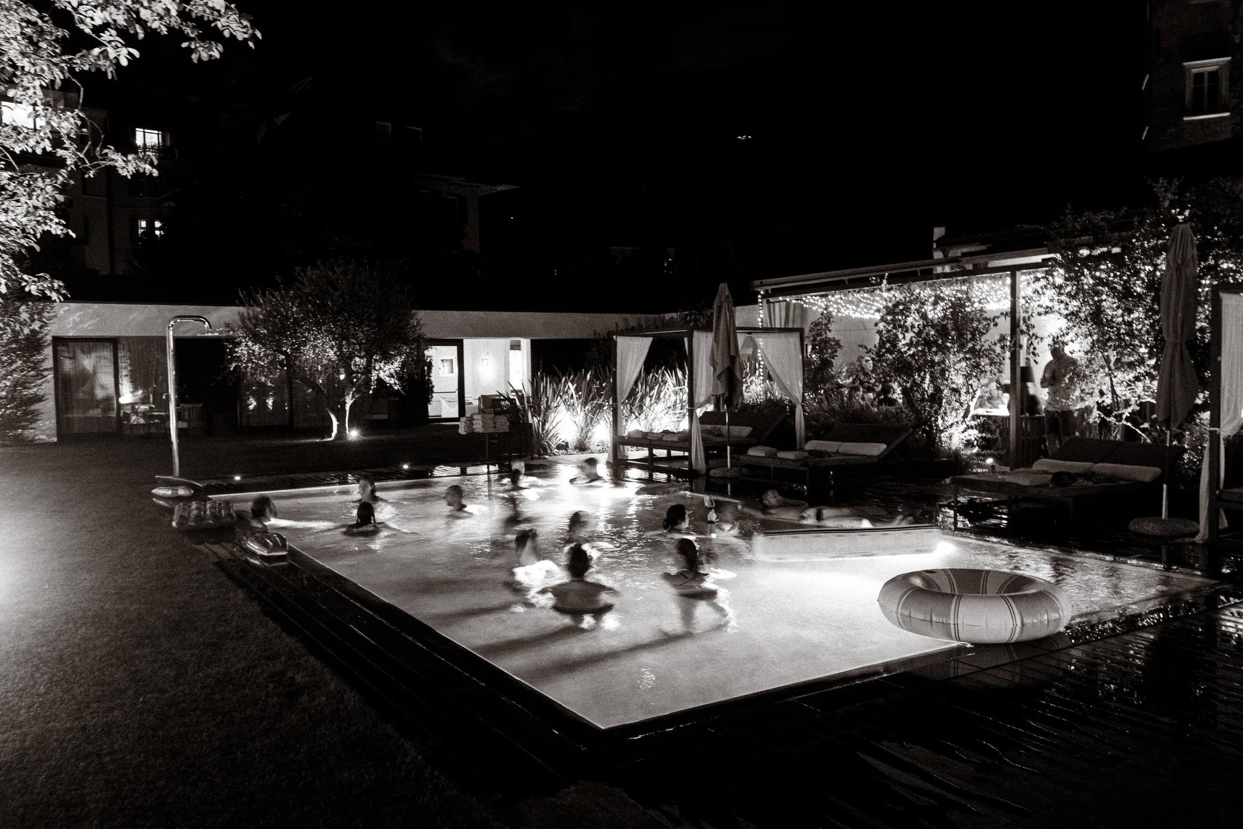 Wedding party guests celebrating and swimming in the pool during a late-night welcome event at Castel Hörtenberg. 