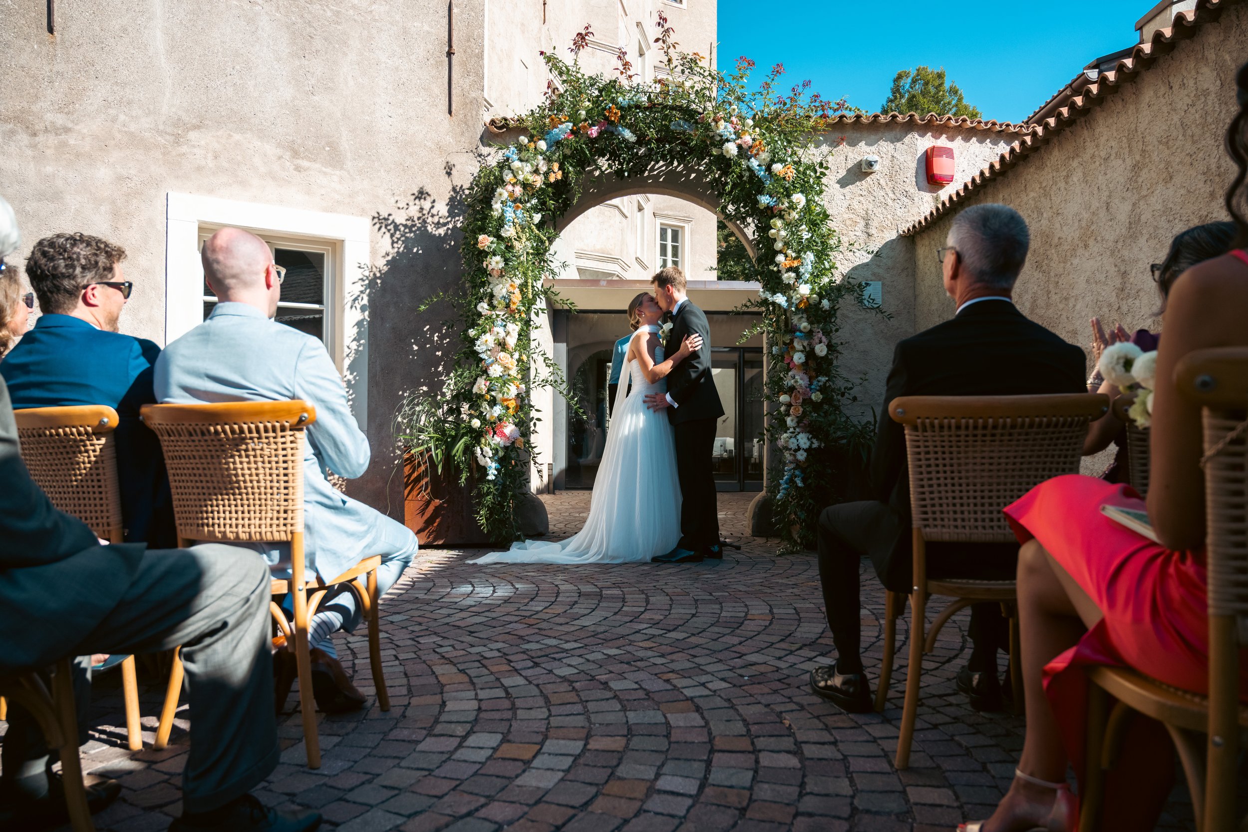  Wide-angle documentary shot of an outdoor destination wedding ceremony taking place on the grounds of Castel Hörtenberg. 