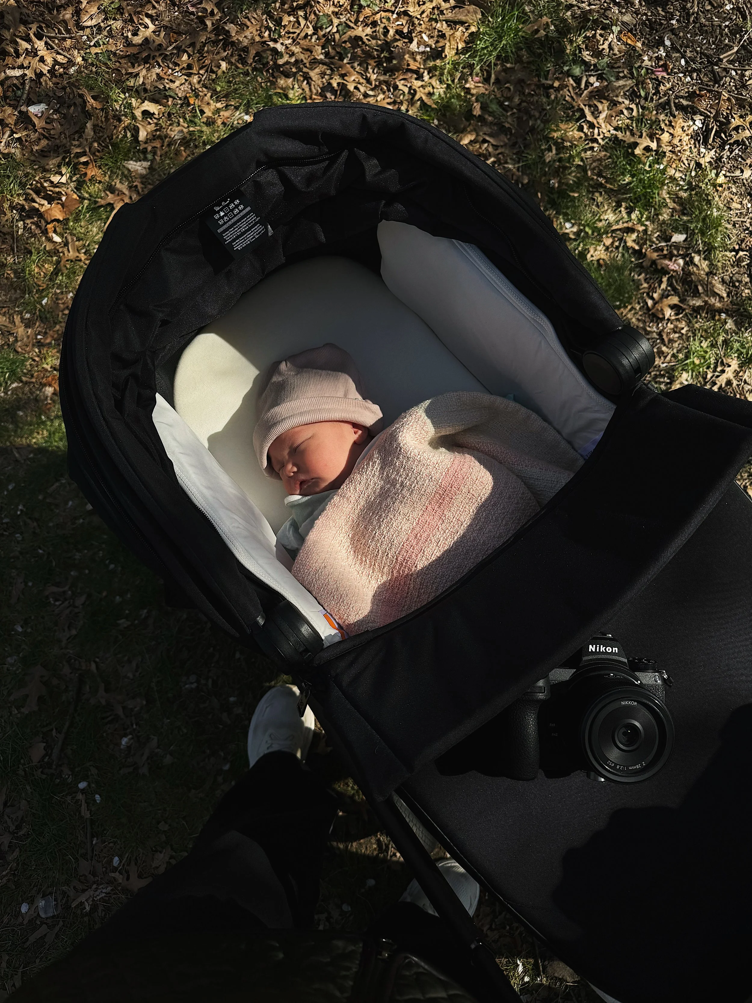 A professional Nikon DSLR camera resting on the canopy of a baby stroller during an outdoor shoot.