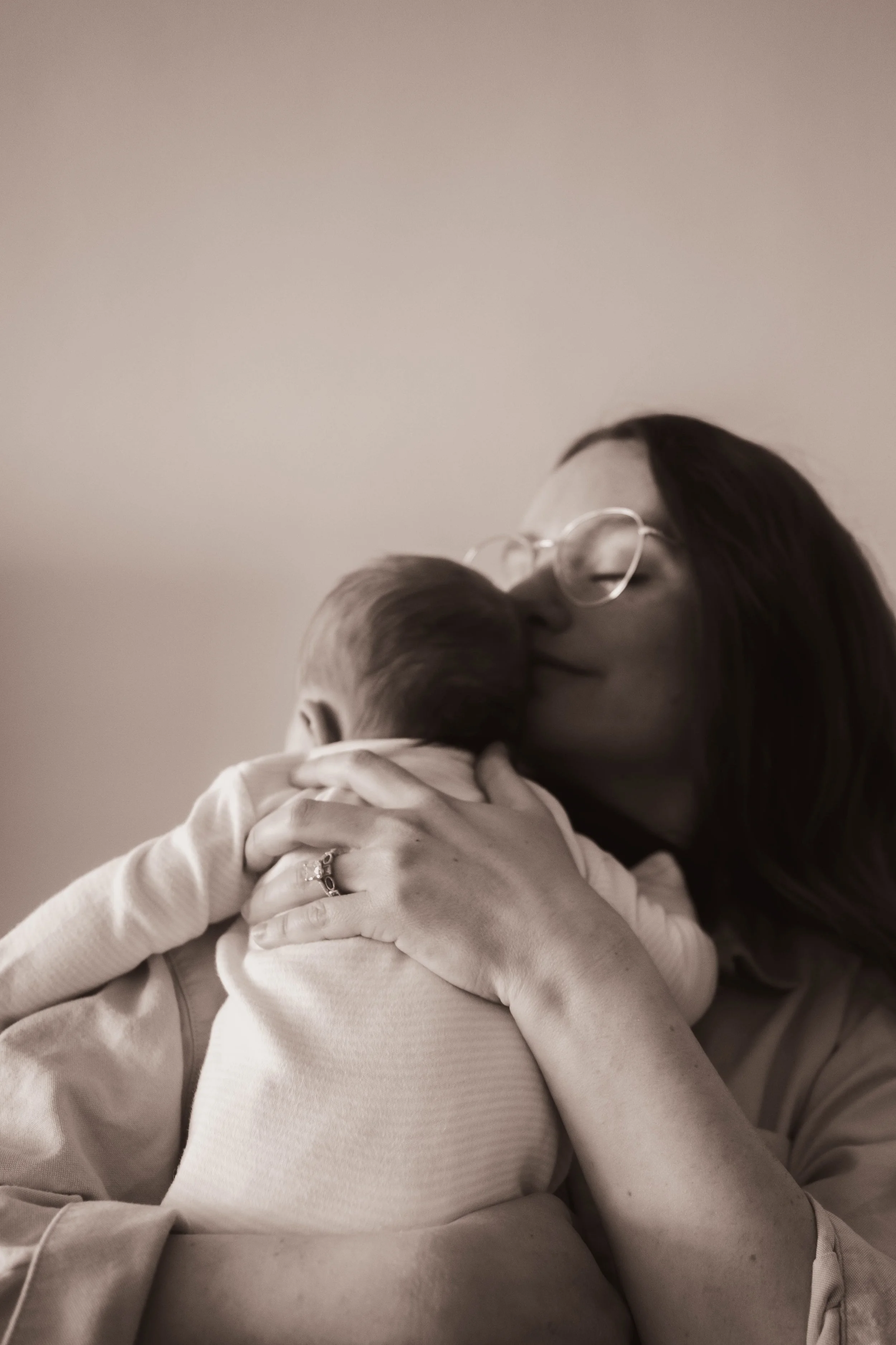 New York City newborn photographer captures an editorial-style portrait of a mother holding her newborn baby against a clean, minimal wall, highlighting natural light and intimate connection.