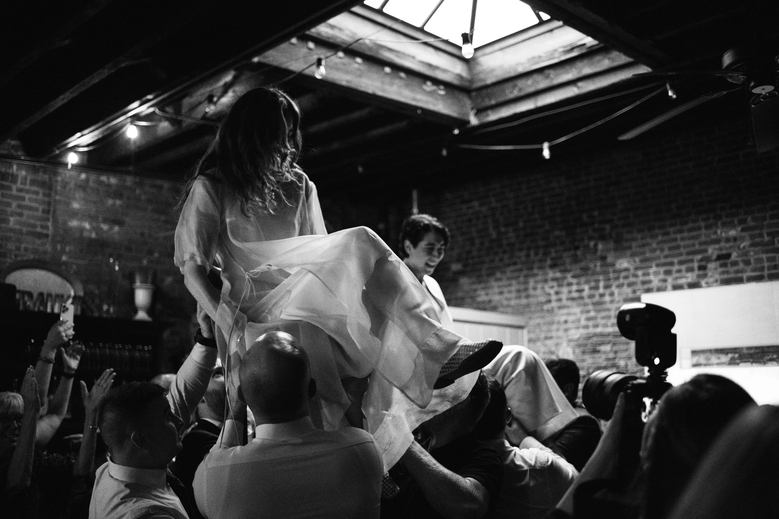 Queer couple being lifted in chairs by guests during their wedding reception