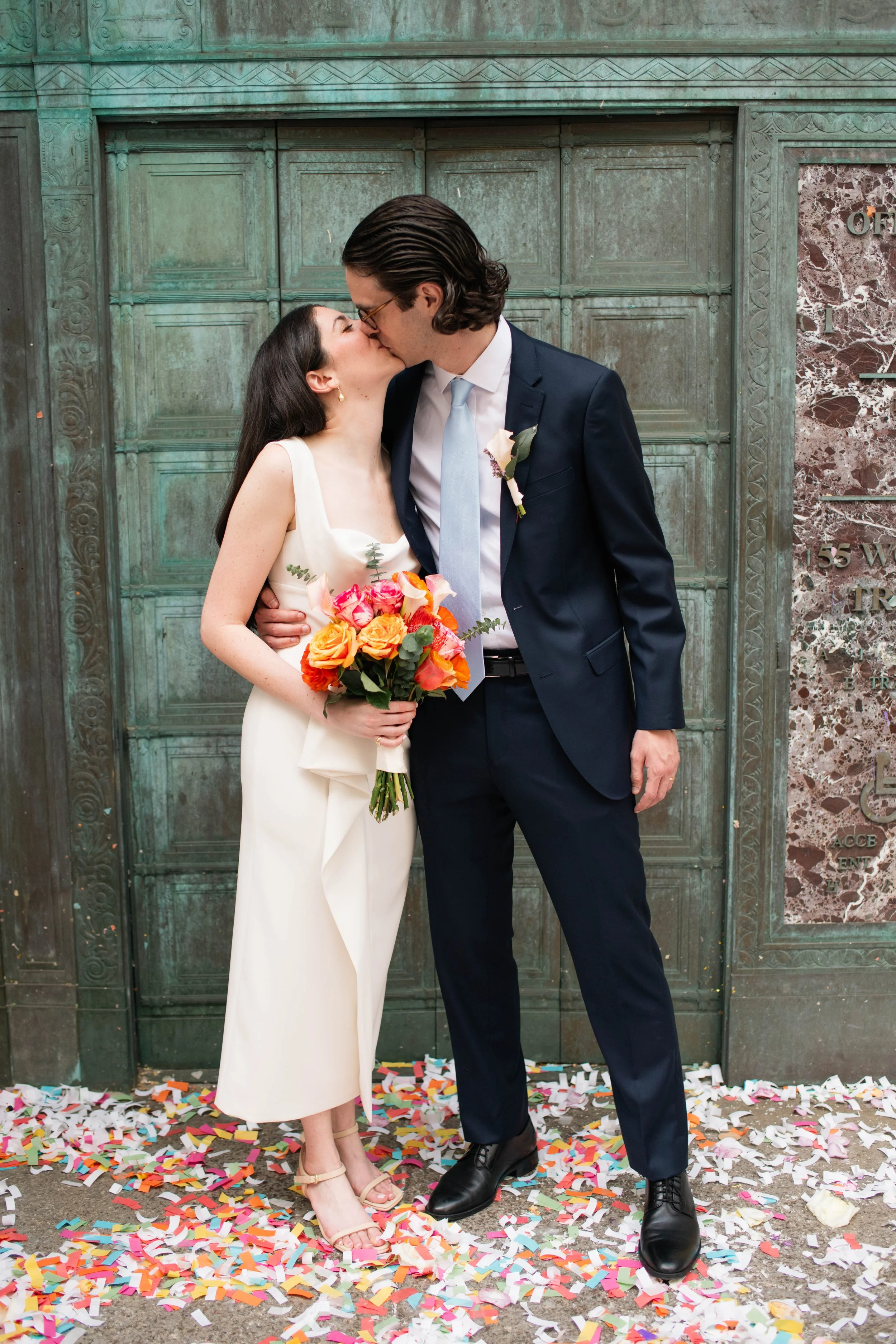 Couple sharing a kiss outside the iconic green doors of the Manhattan courthouse after their wedding