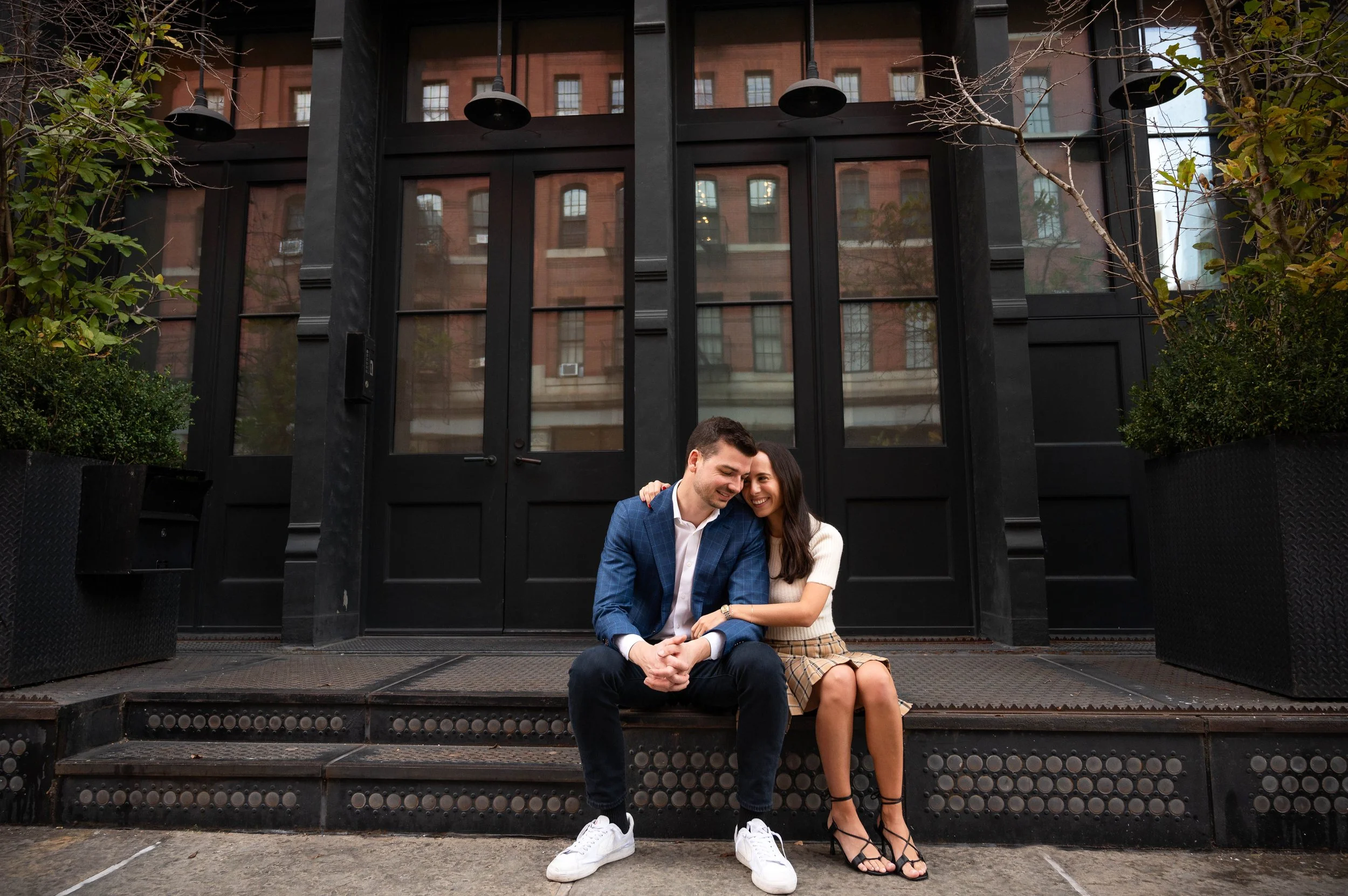 Couple sitting on a stoop in Tribeca smiling at each other during an engagement photoshoot