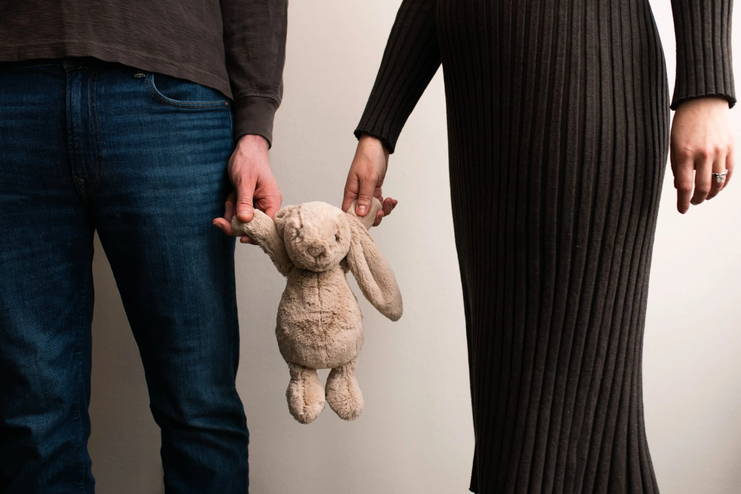 Pregnant NYC photographer and her husband each holding the hand of a stuffed bunny in a sweet pregnancy announcement photo, New York City